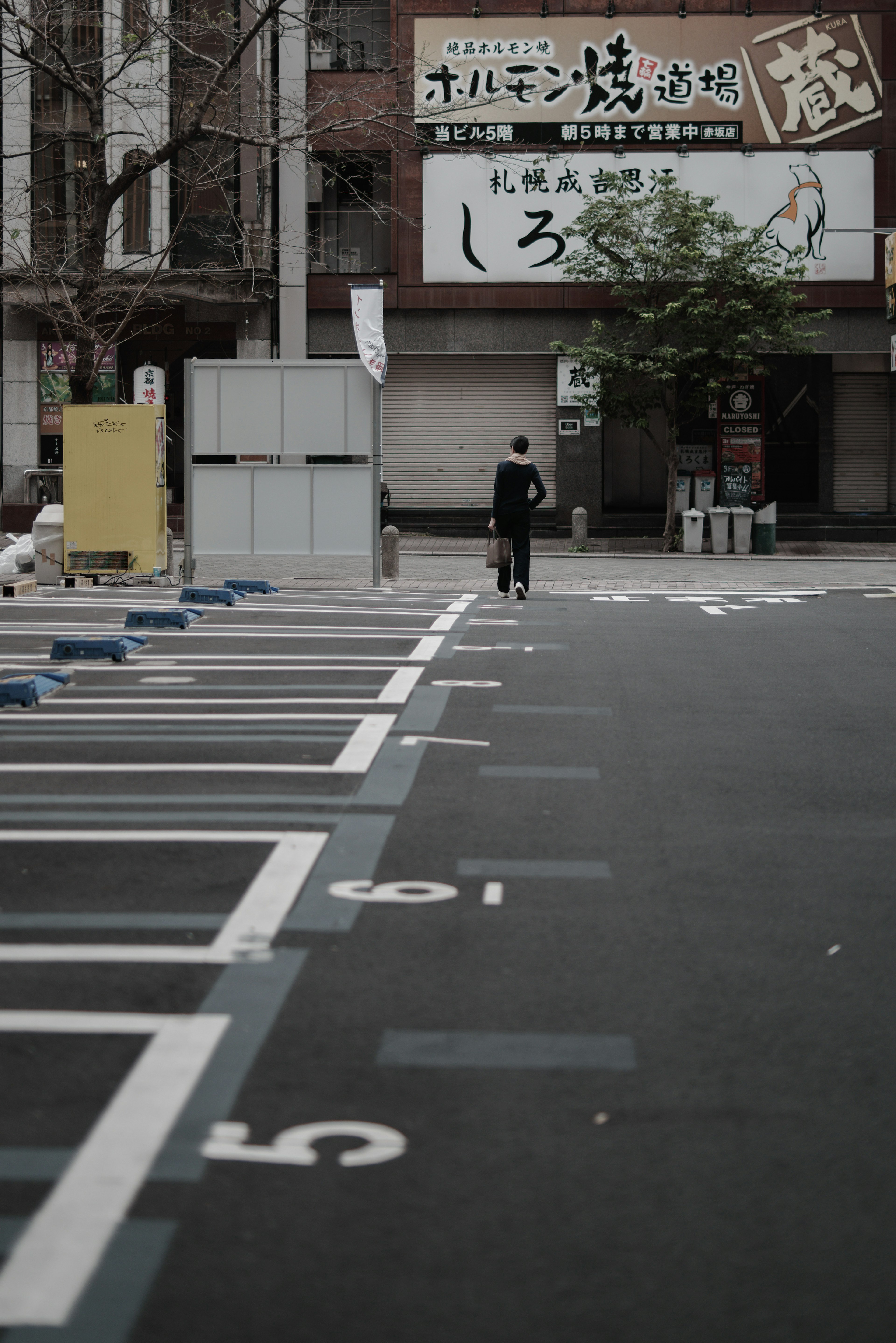 一個人在空曠的停車場走，背景是商業建築的招牌