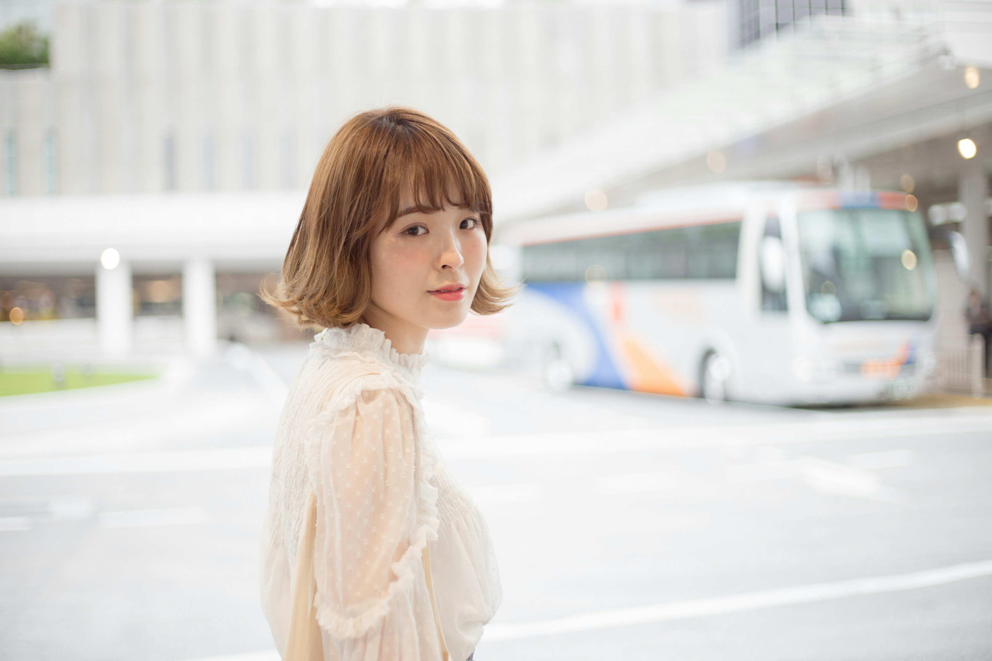 Young woman looking back at a bus stop wearing a white blouse and brown hair with a colorful bus in the background