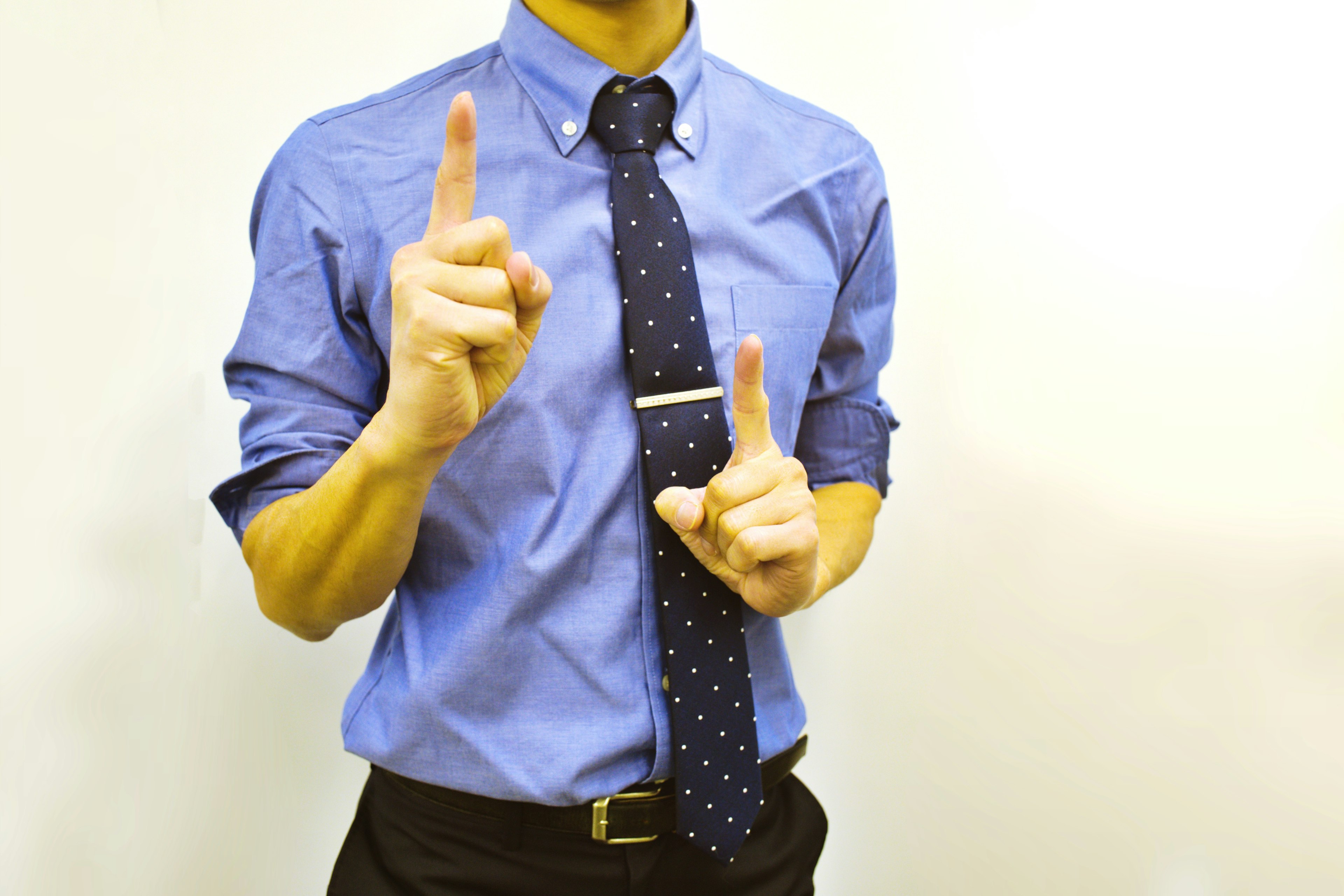 Un uomo in camicia blu e cravatta a pois che alza un dito