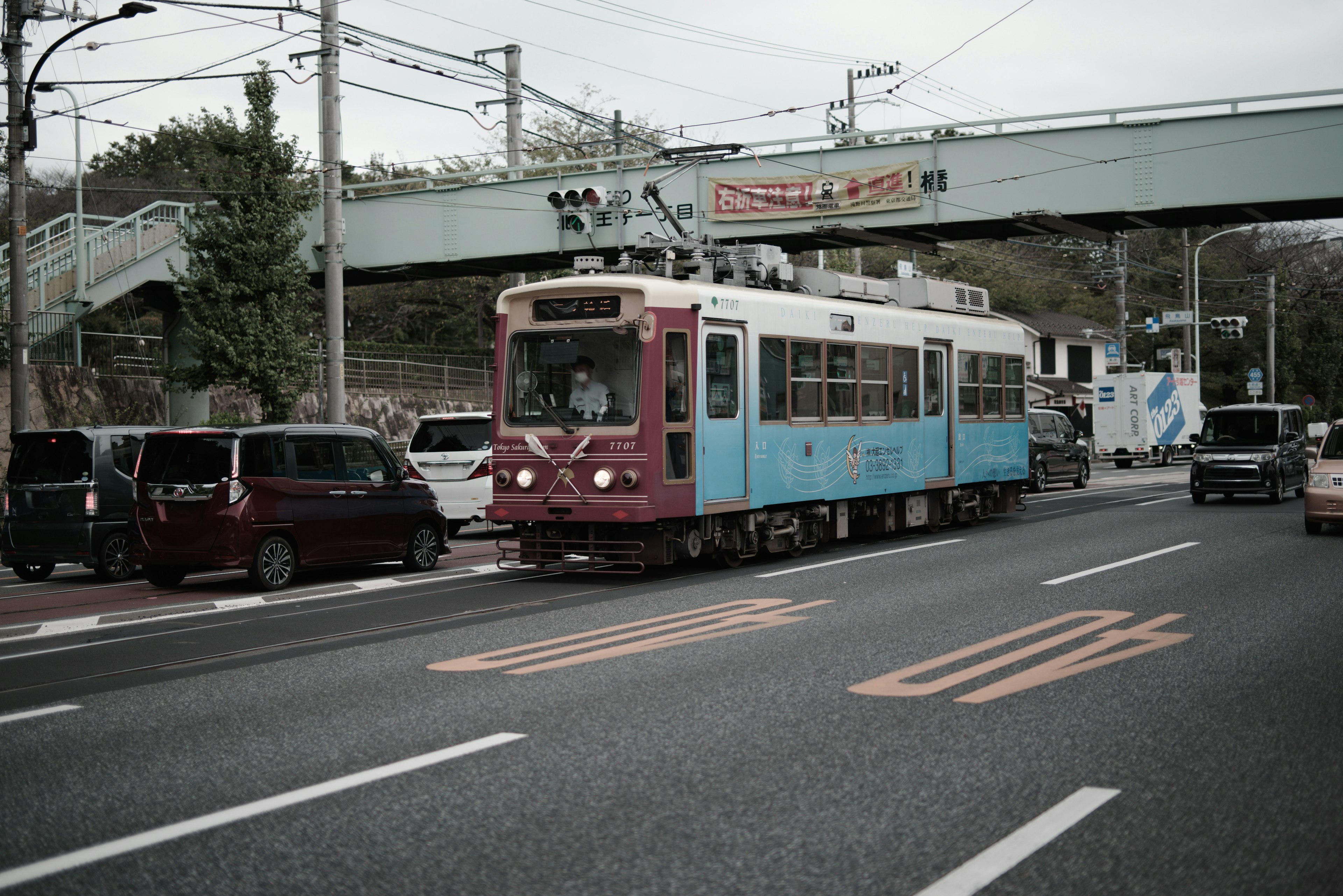 一輛藍色和紅色的電車在道路上行駛，周圍停著汽車