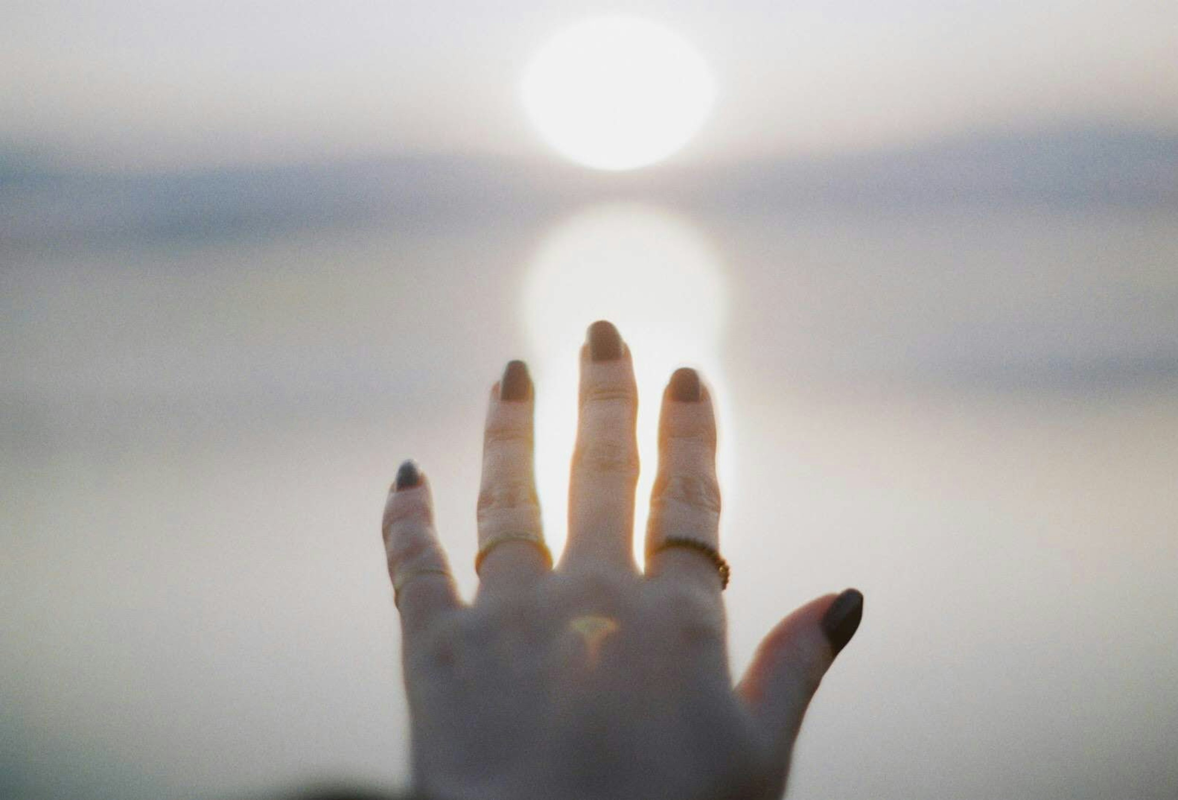 Eine Hand, die sich zur Sonne streckt, mit verschwommenem Hintergrund von Ozean und Himmel