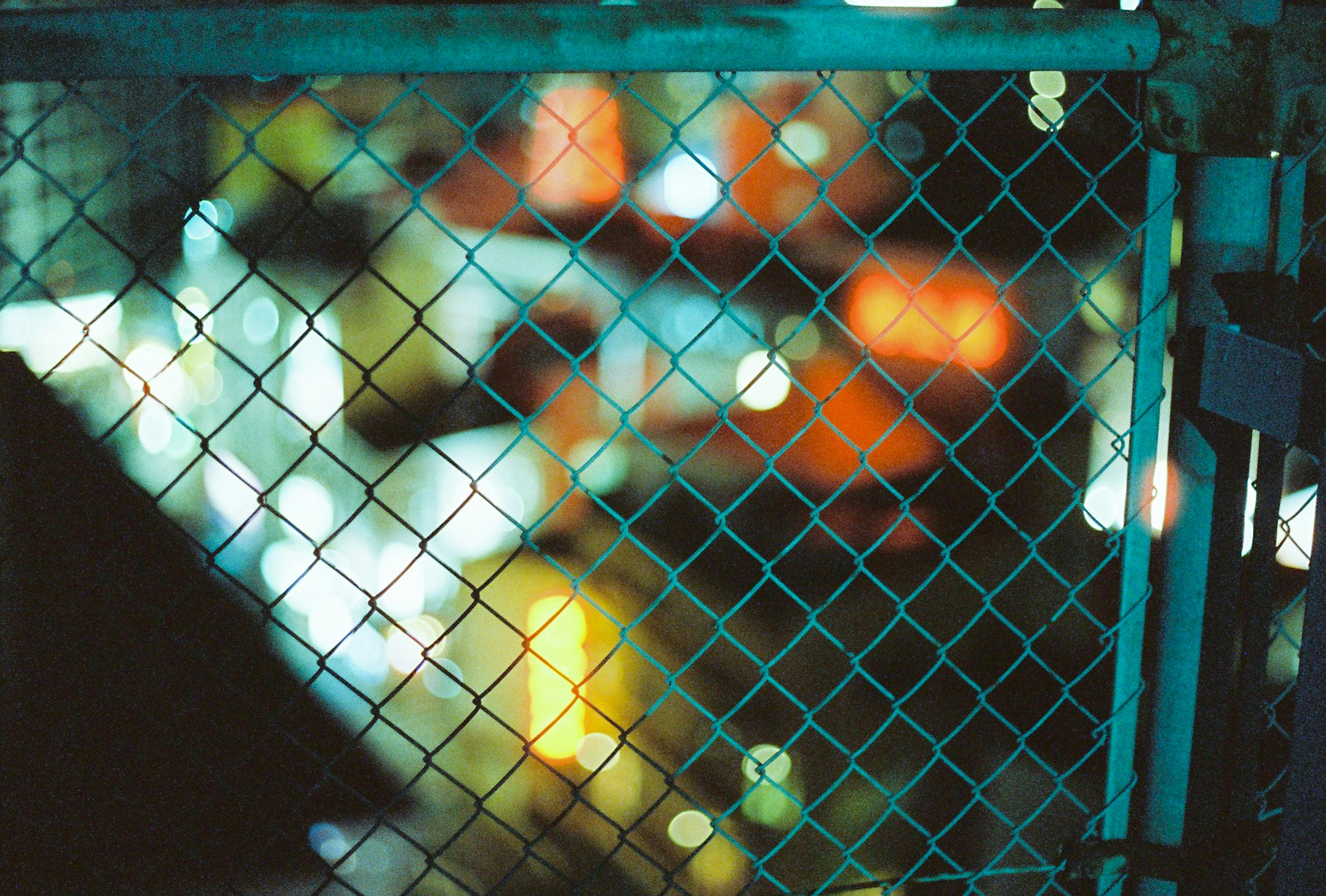 A blurred background with a mesh fence featuring colorful lights reflecting through it