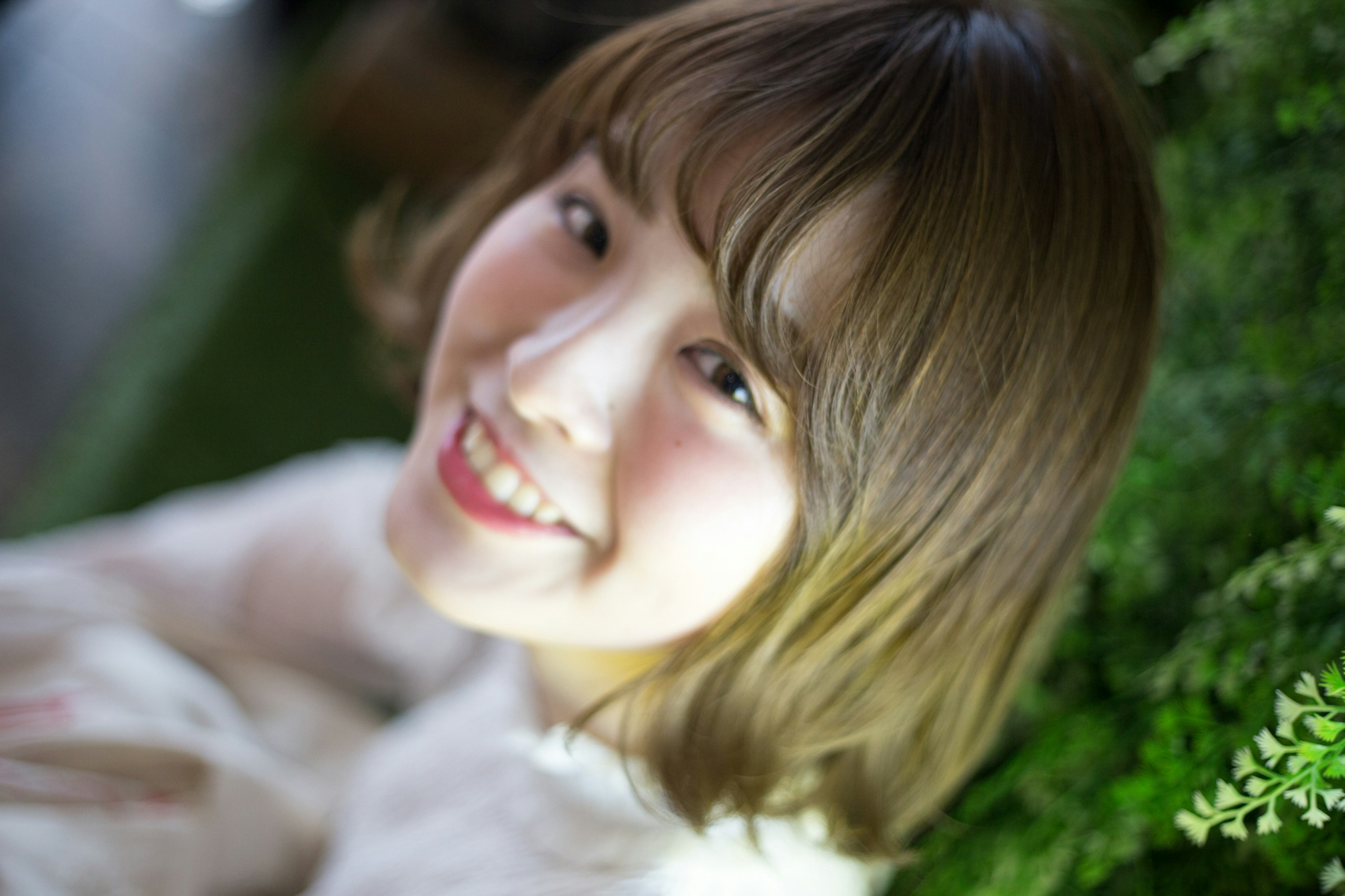 Portrait of a smiling woman sitting in front of green plants with soft lighting