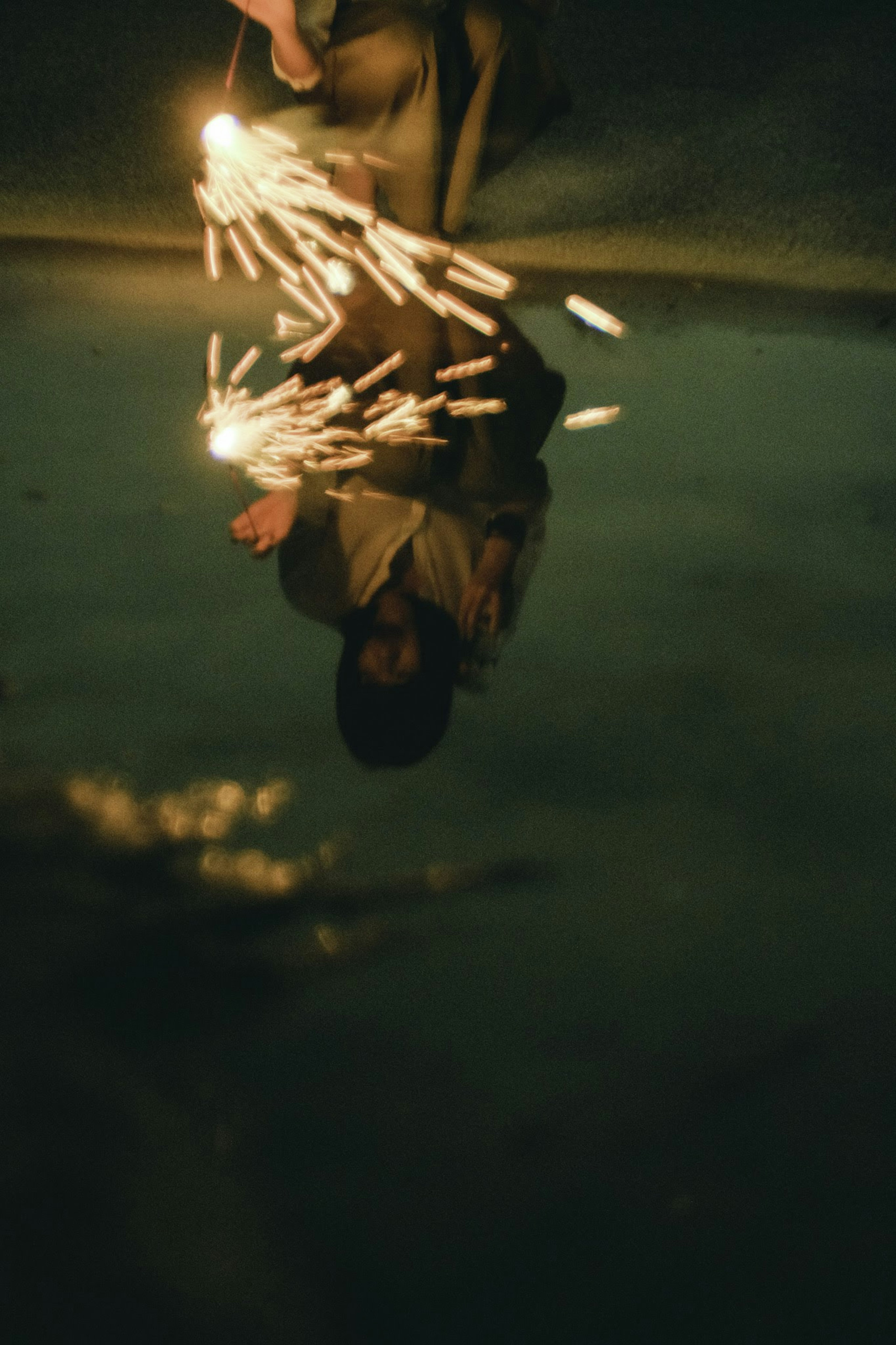 Child holding sparklers reflected in water