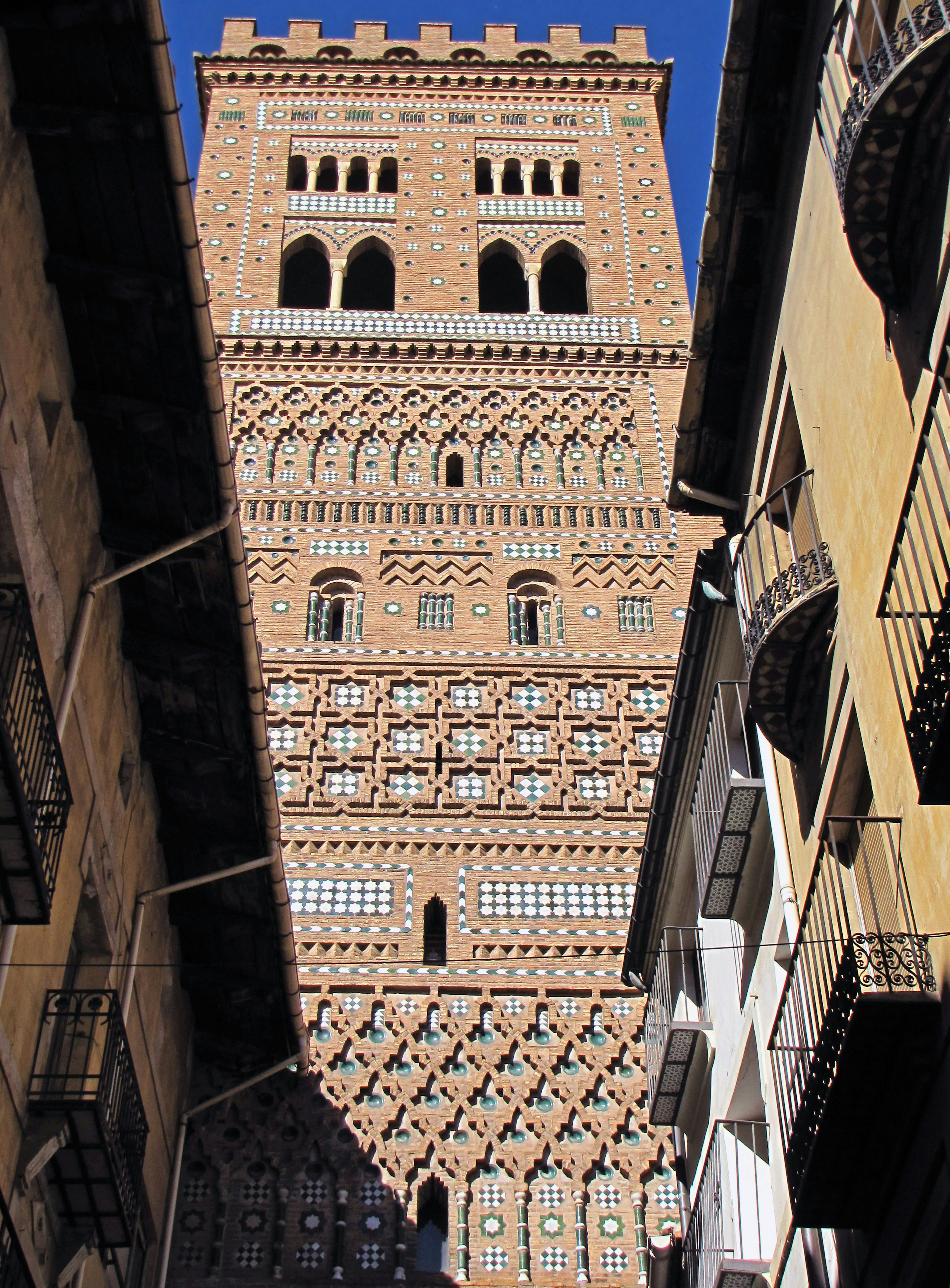 Alta torre de ladrillo con intrincadas decoraciones se eleva sobre una calle estrecha