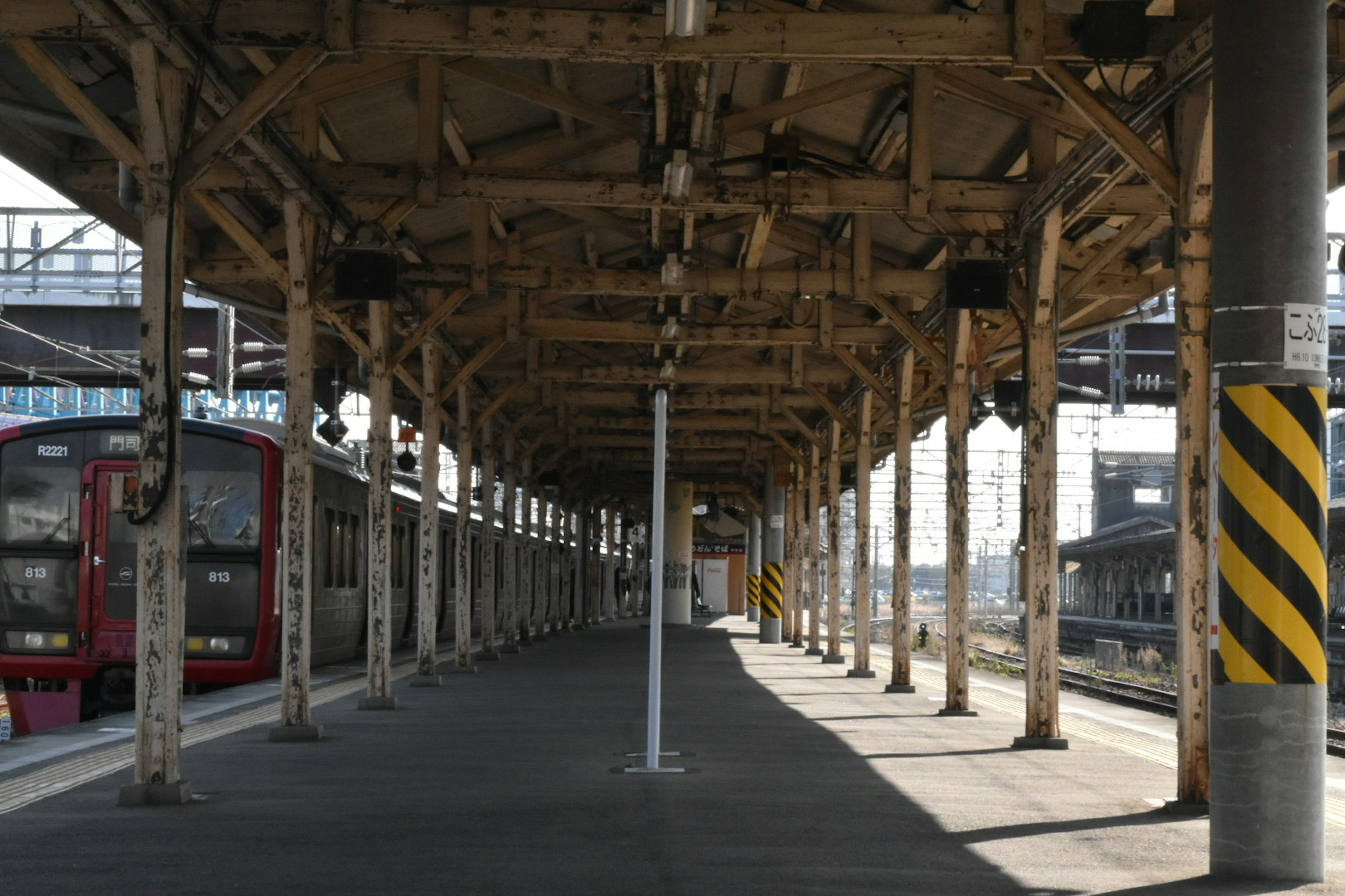 ทิวทัศน์ของชานชาลาสถานีรถไฟพร้อมเพดานและเสาไม้มีรถไฟสีแดงมองเห็นได้