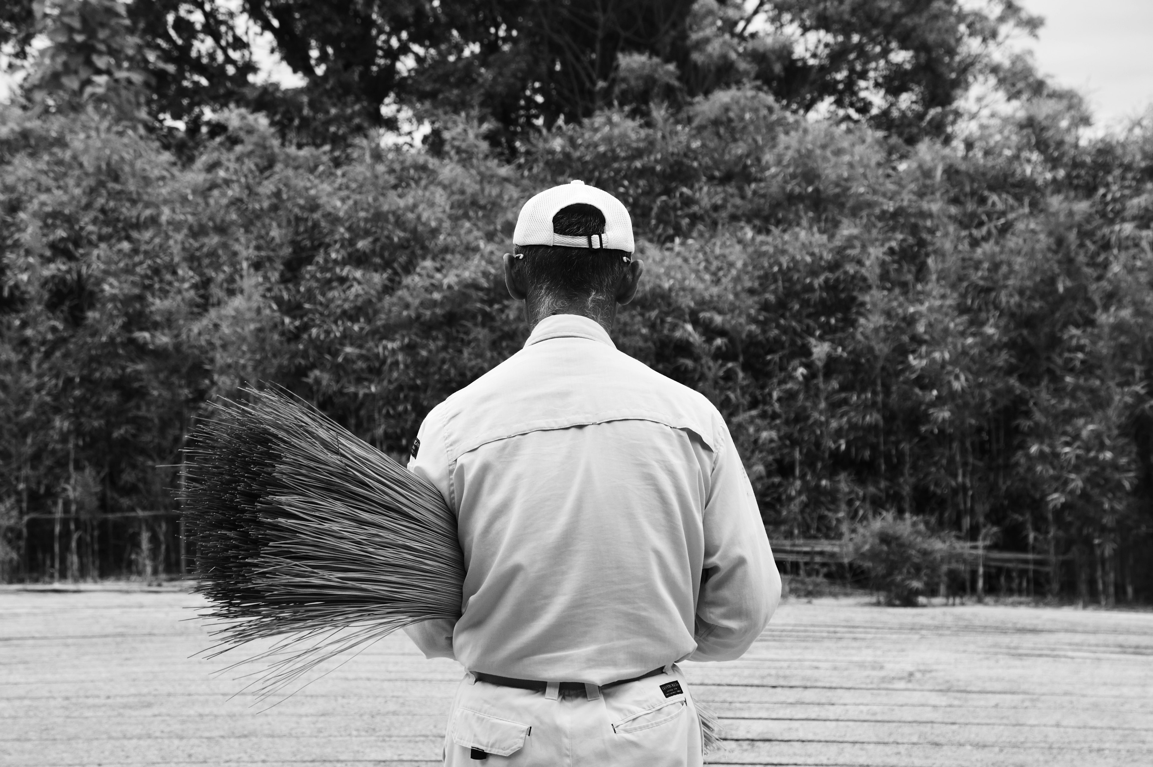 Un homme tenant un balai vu de dos dans une image en noir et blanc