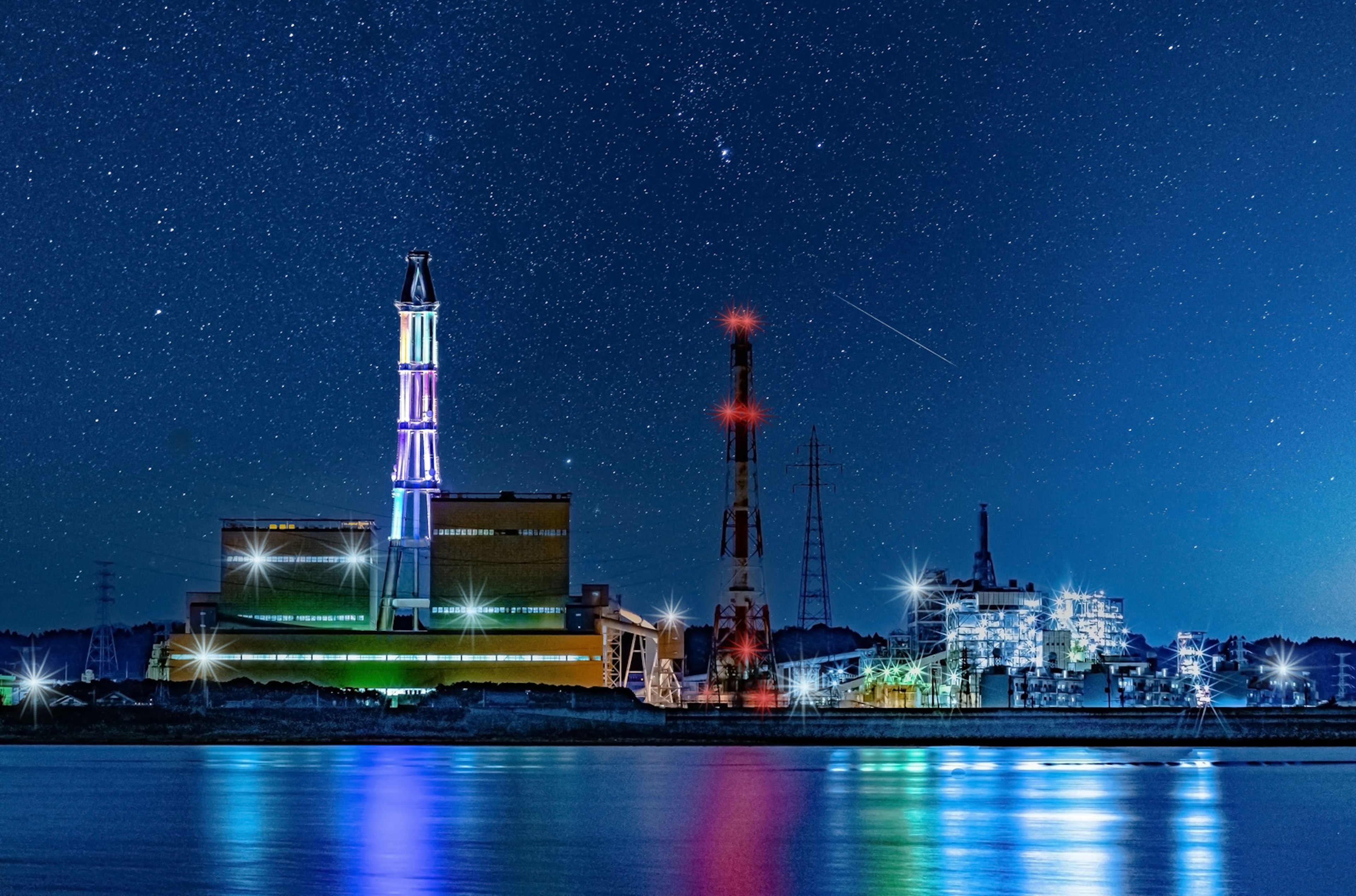 Industrial facility illuminated at night with stars in the sky and reflections on the water