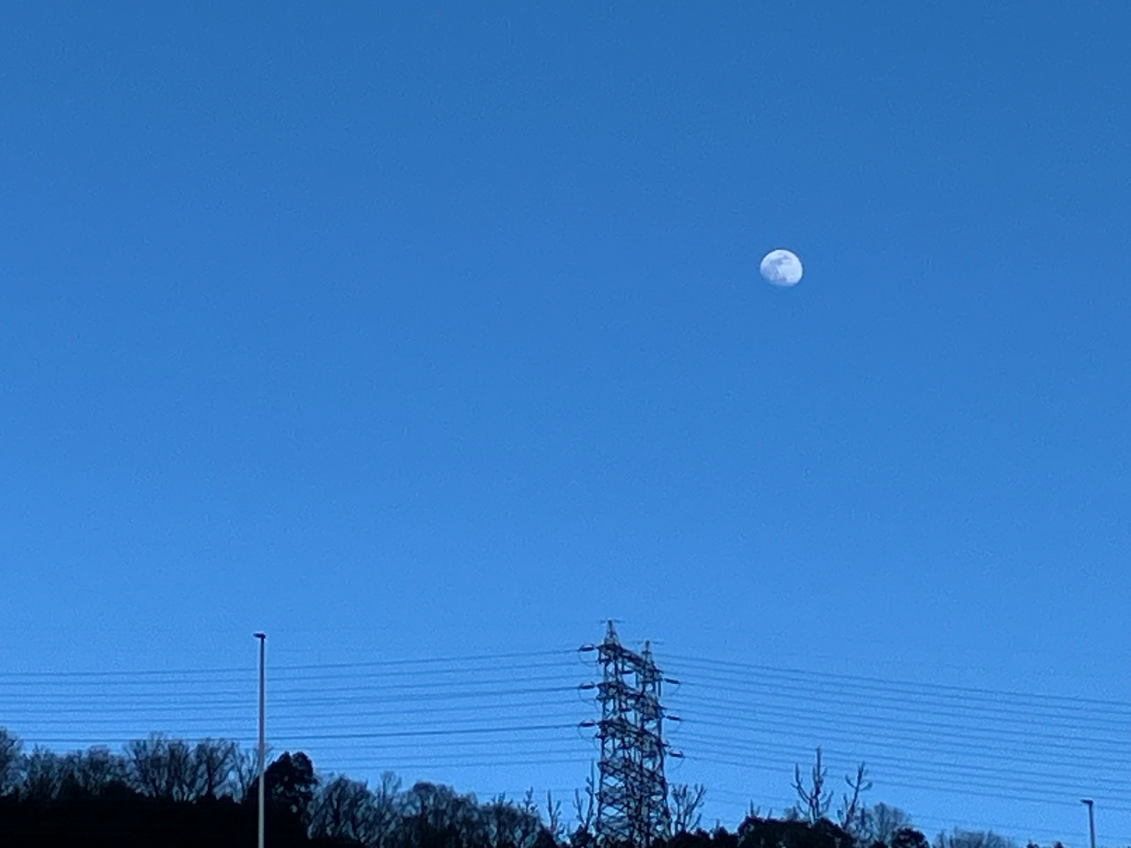 Pemandangan bulan di langit biru dengan saluran listrik di latar depan