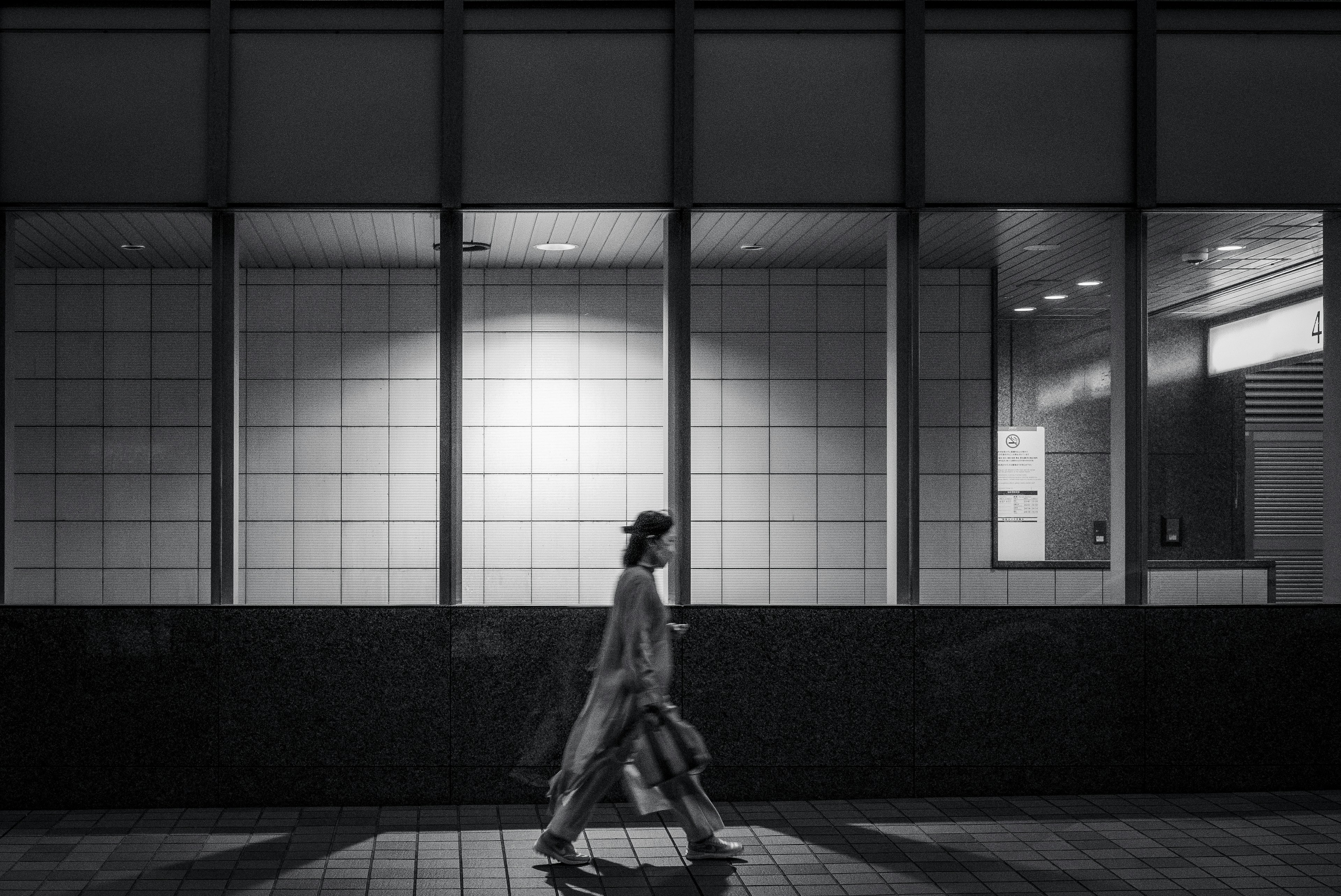 A woman walking in a nighttime urban setting with a monochrome background and large windows