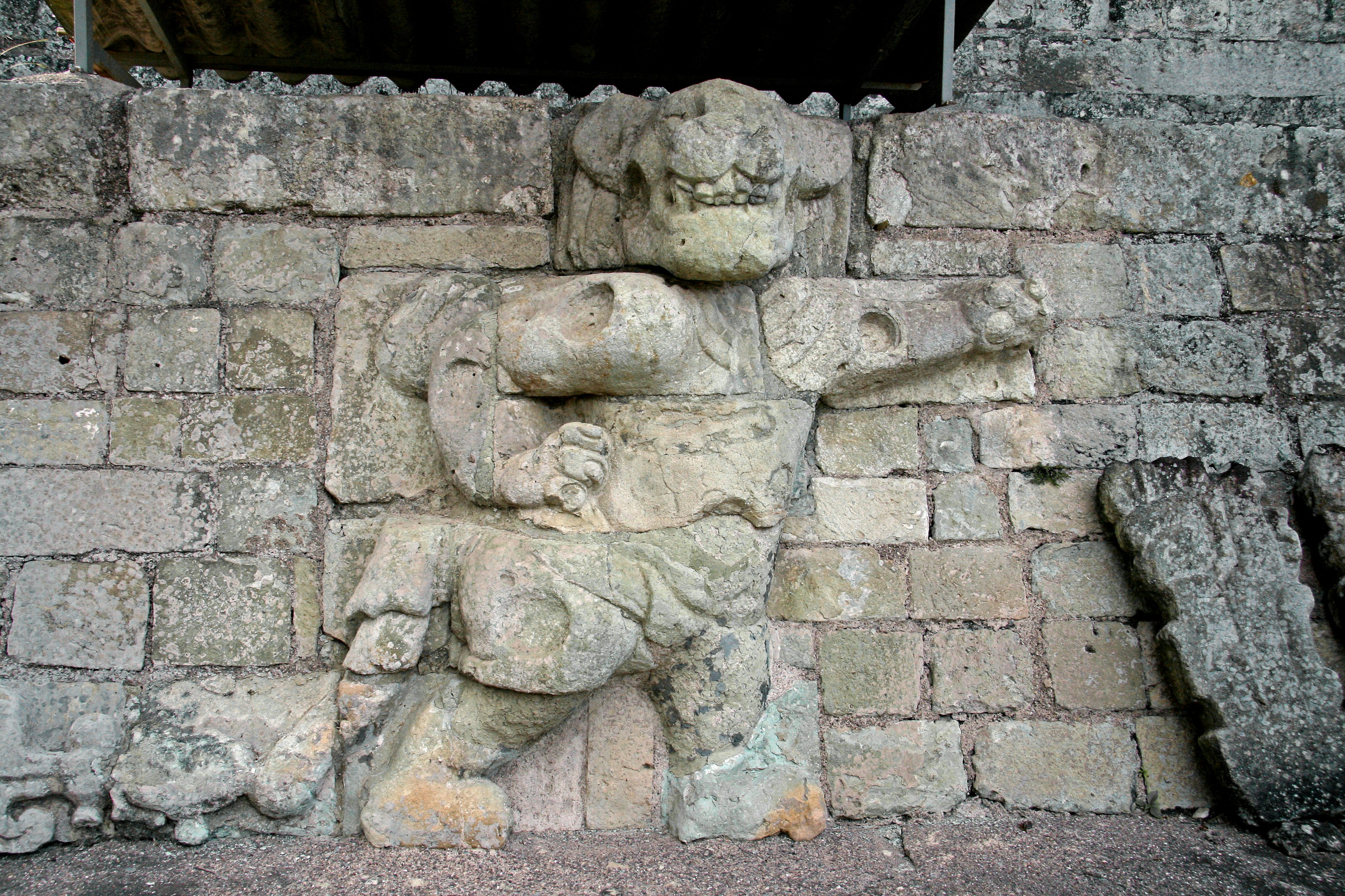 Estatua antigua de piedra tallada en la pared con una postura poderosa y la mano levantada