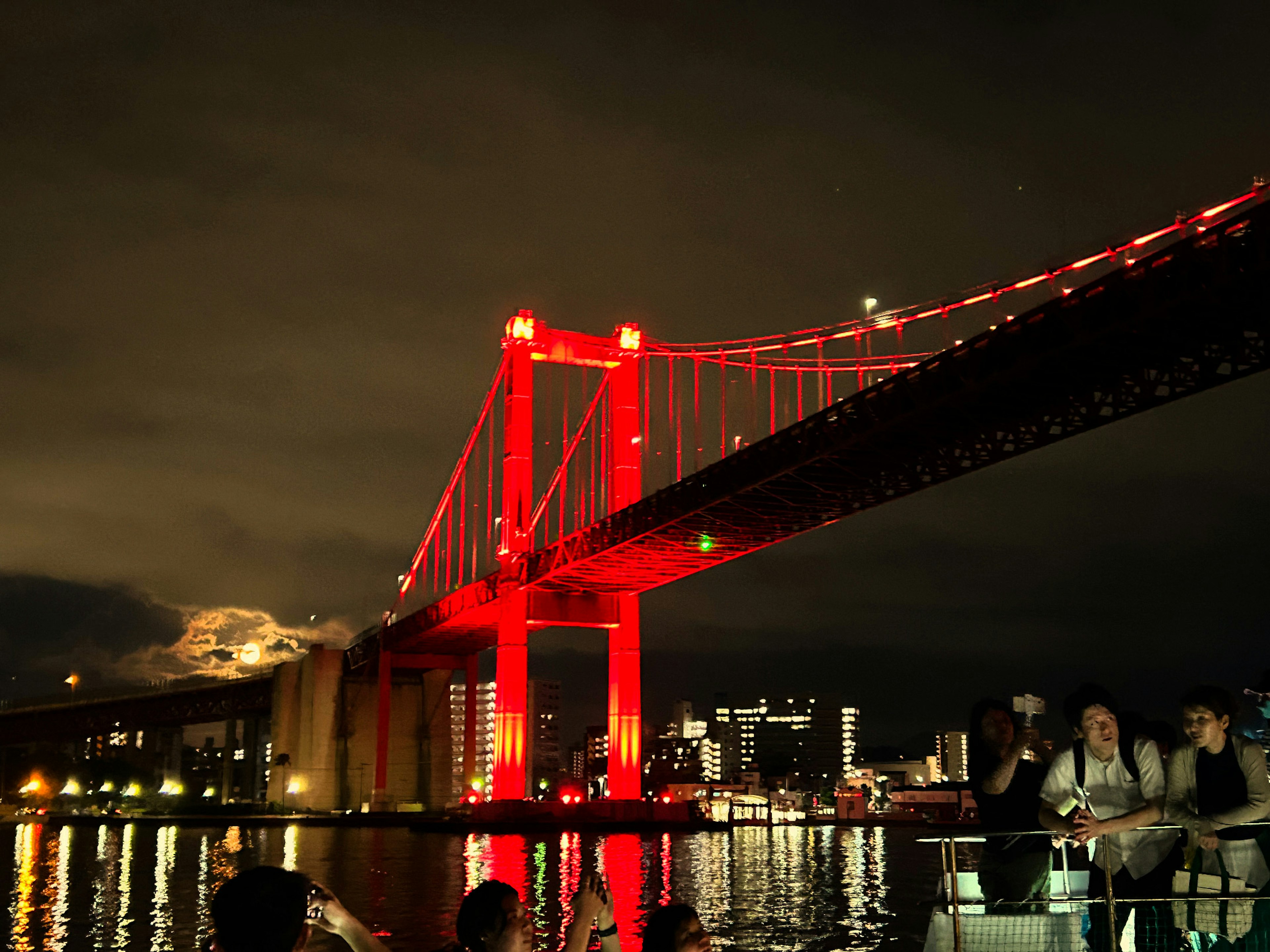 Puente rojo iluminado por la noche con luces de la ciudad reflejadas en el agua