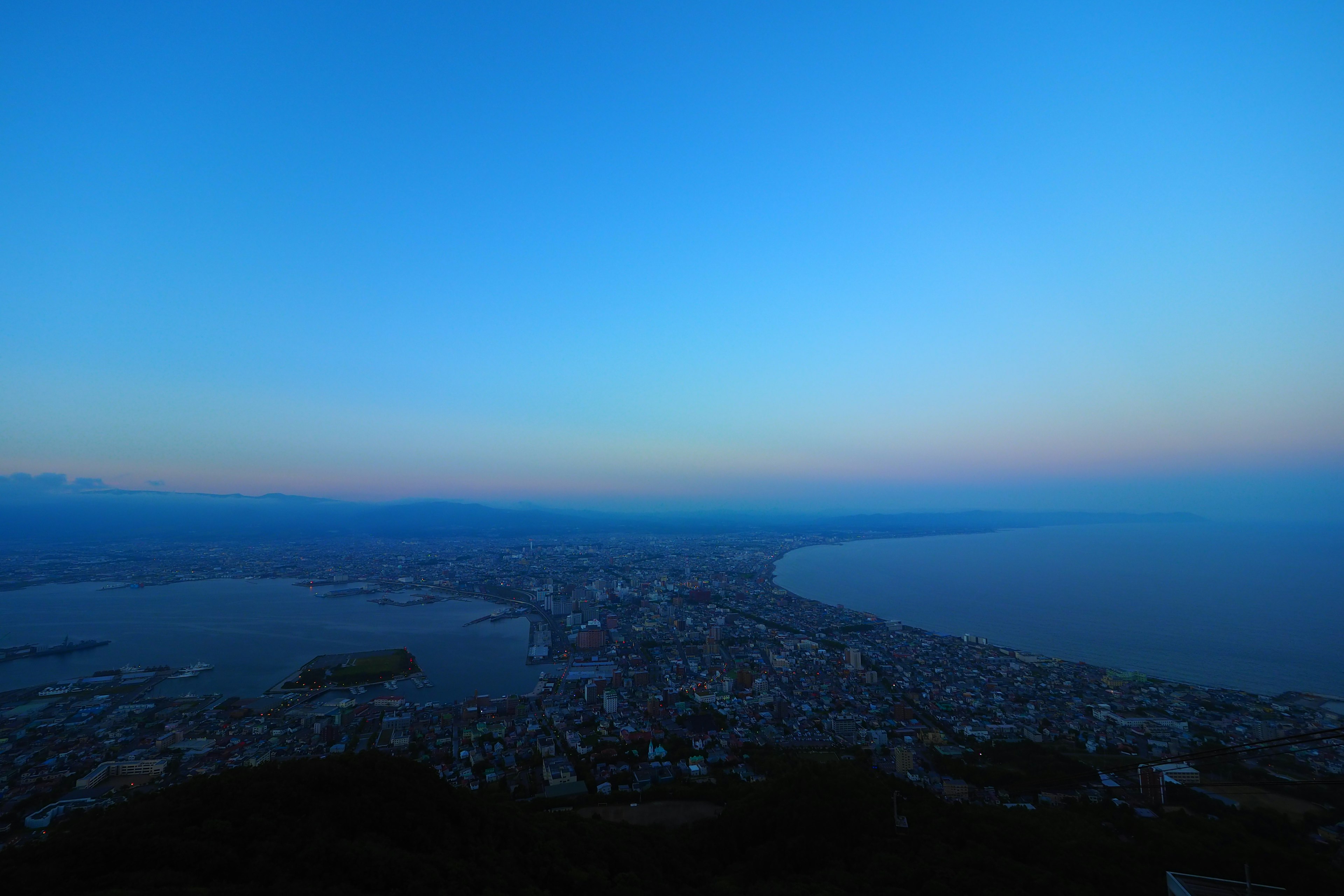 Panoramic view of a coastal city at dusk with blue sky