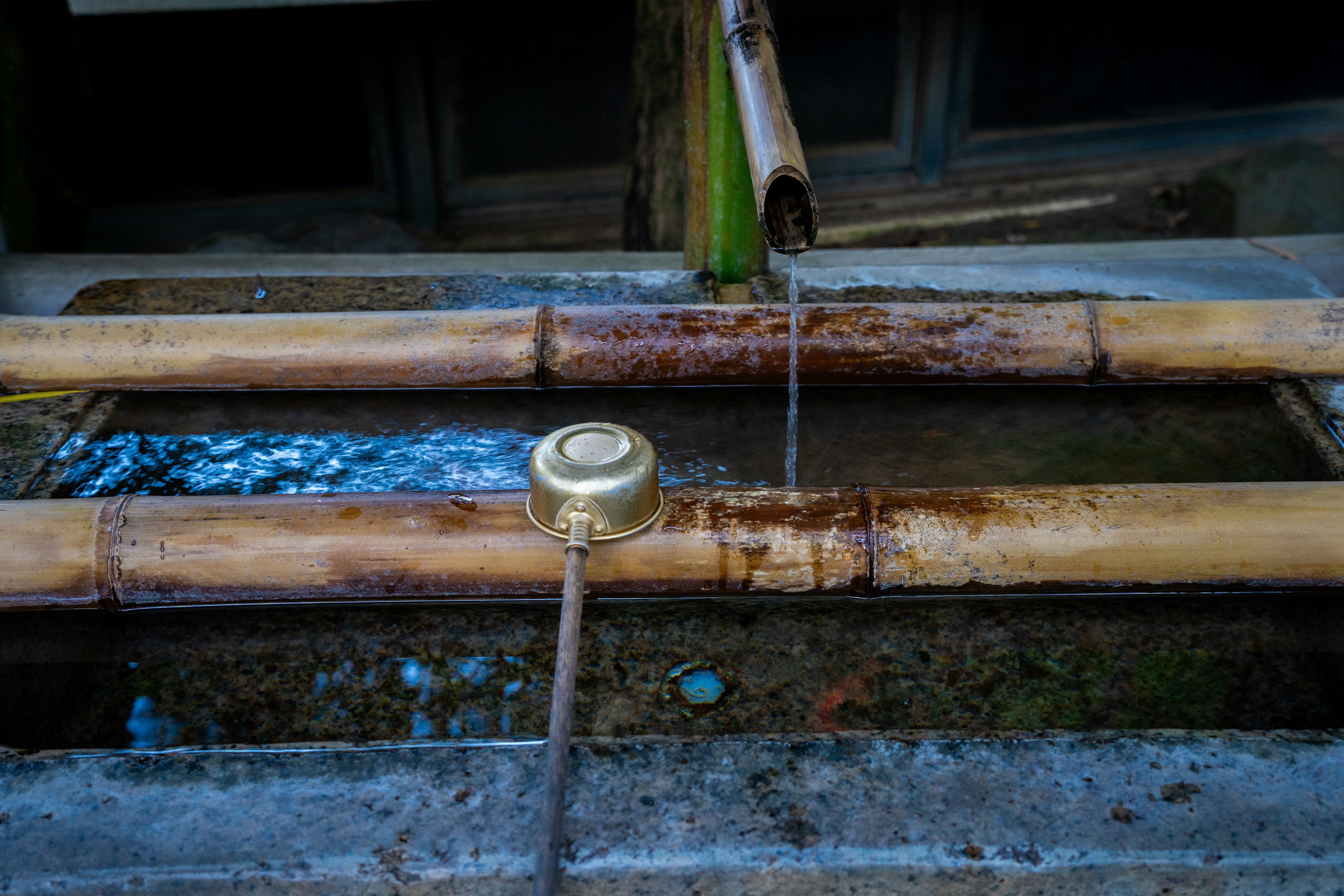 Fontaine d'eau en bambou avec une louche en métal et de l'eau qui coule