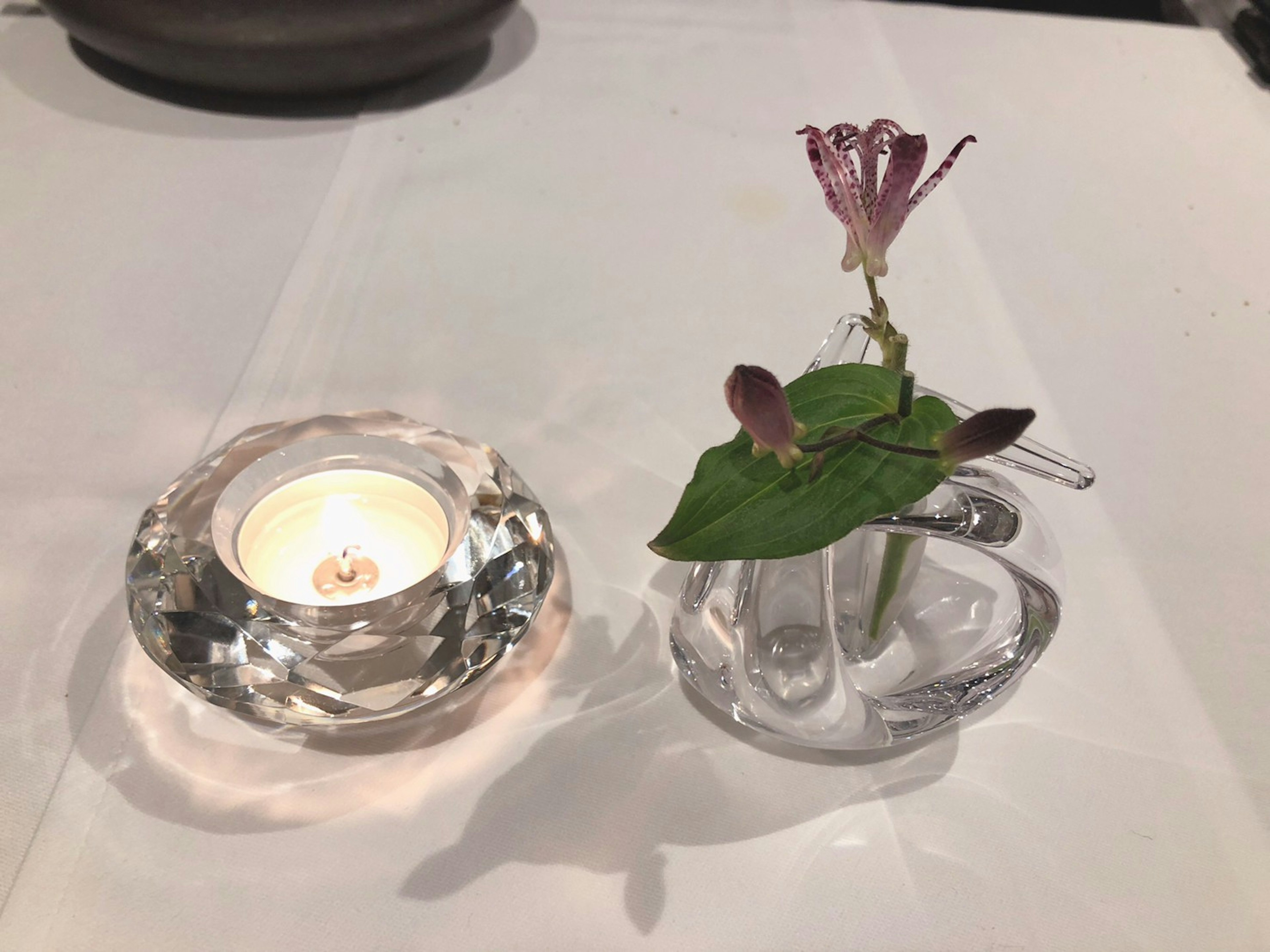 Una vela y un pequeño jarrón con una flor sobre una mesa