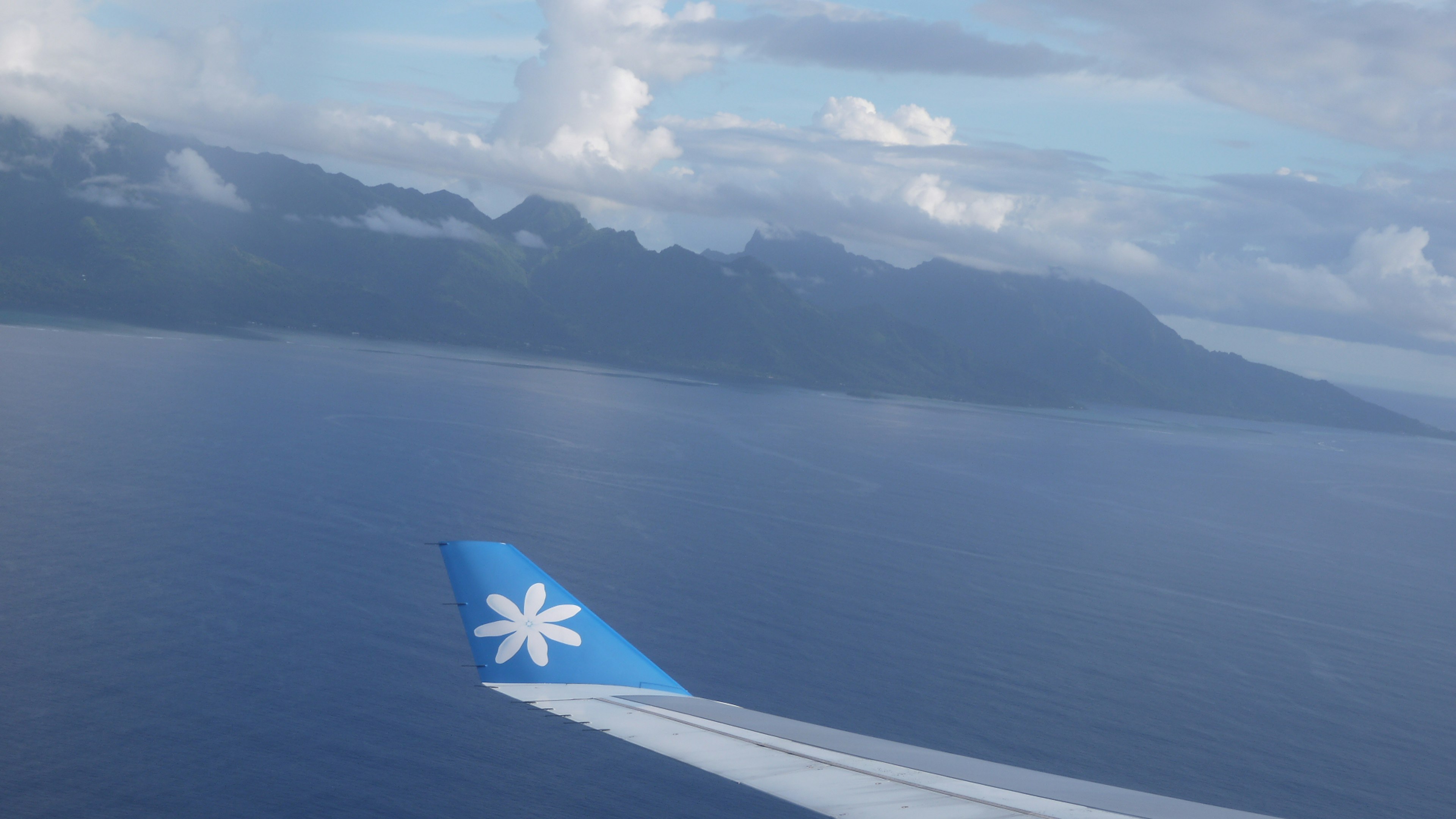 Airplane wing over blue ocean and mountainous landscape