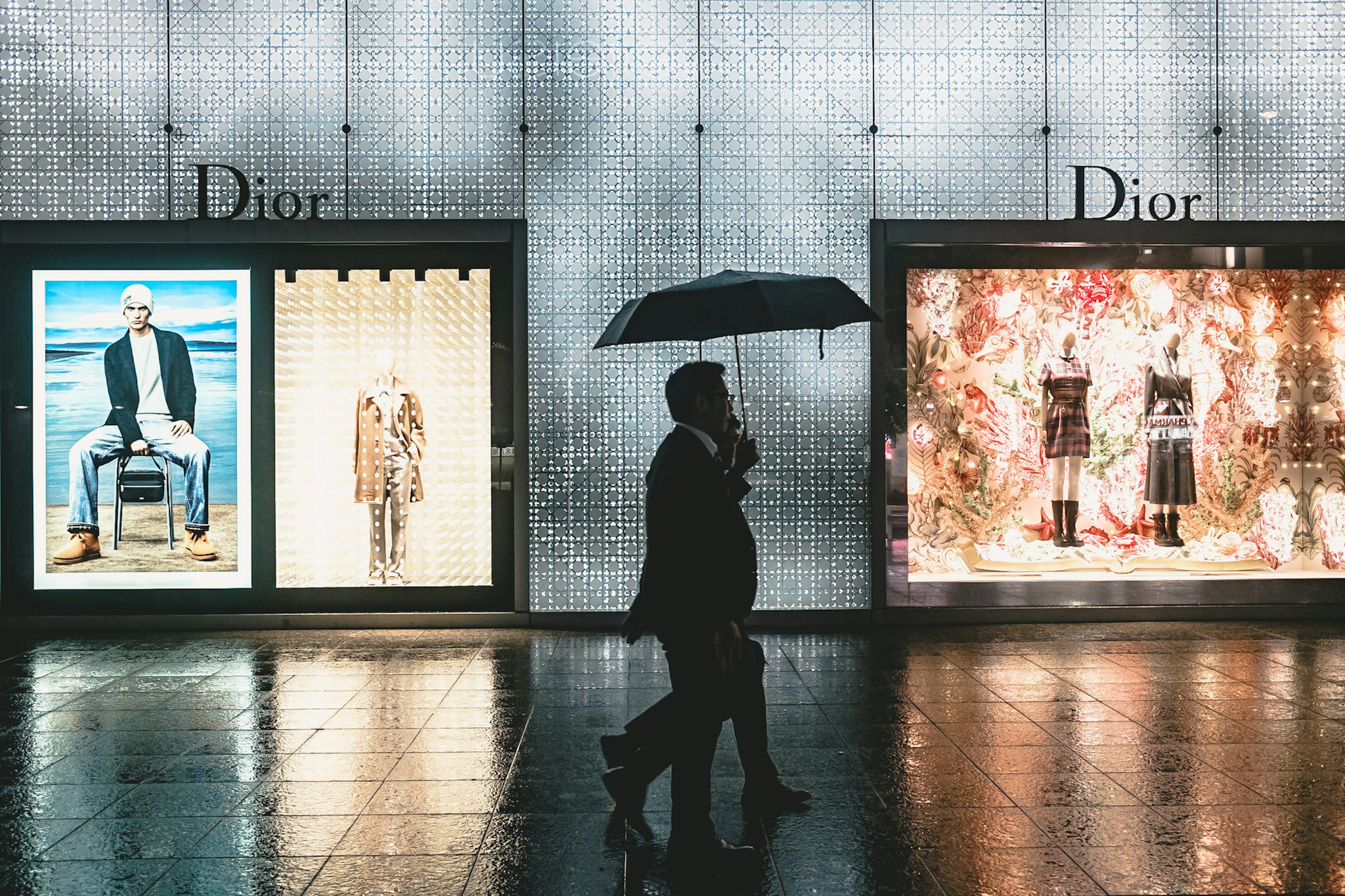 Silhouette einer Person, die mit einem Regenschirm vor Dior-Schaufenstern geht