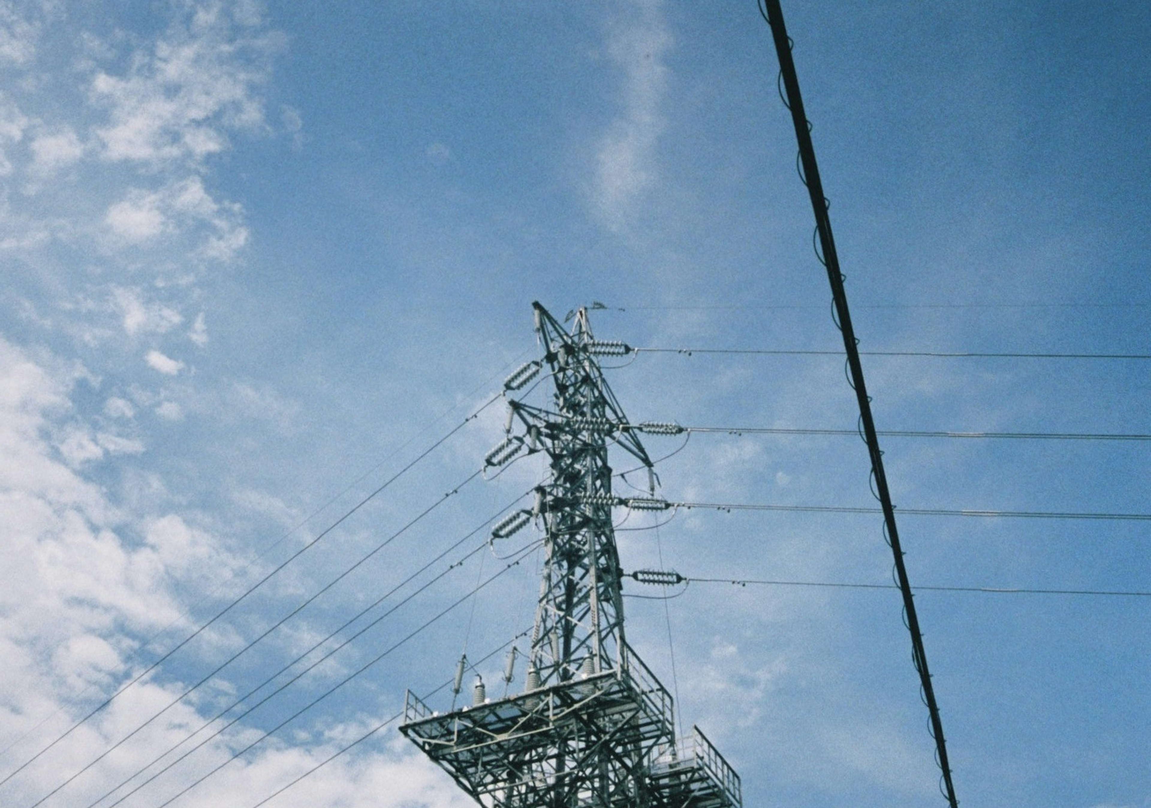 青空の下にある高圧電線の鉄塔