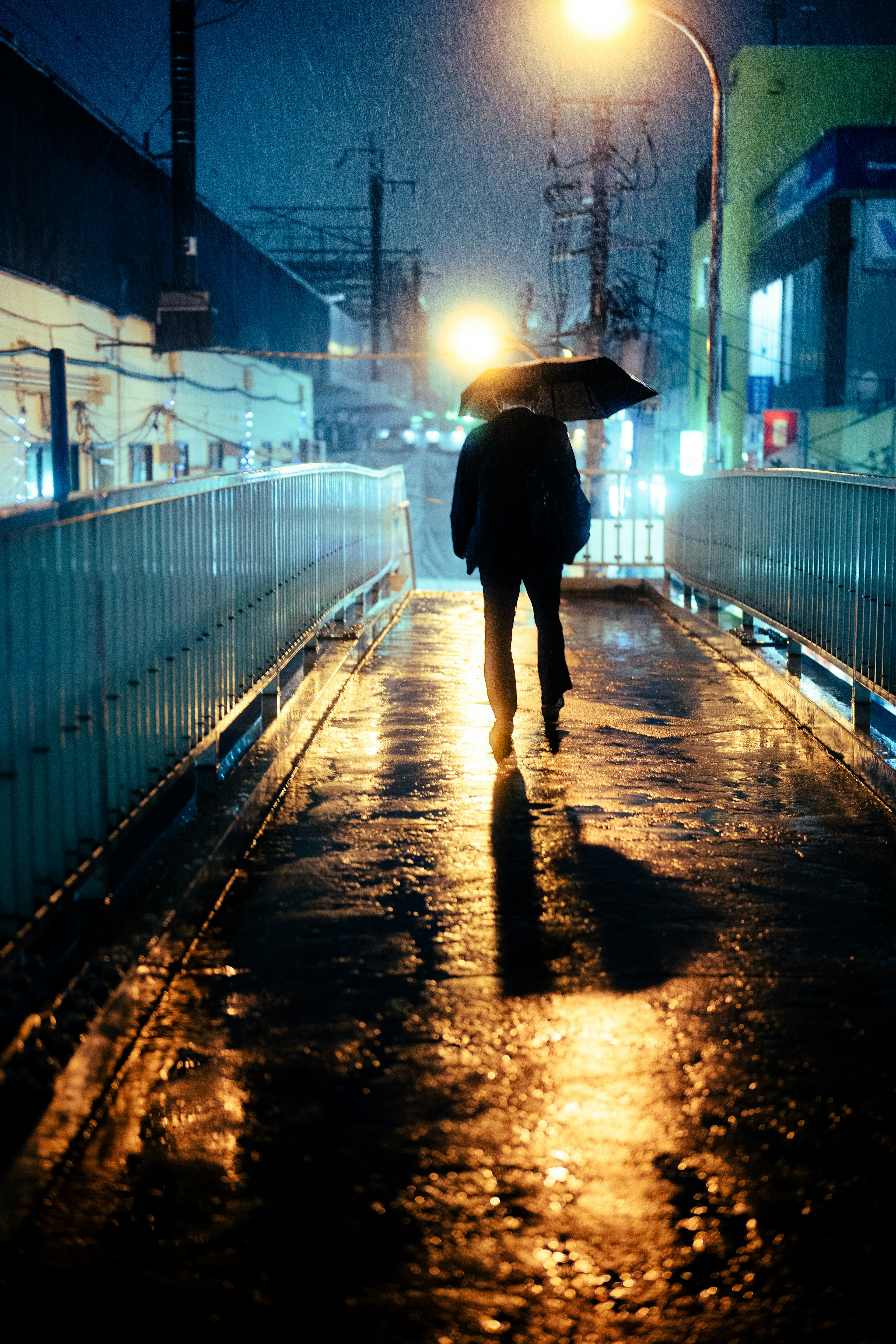 비 오는 날 우산을 쓴 사람의 실루엣 도로 조명이 젖은 보도에 반사됨