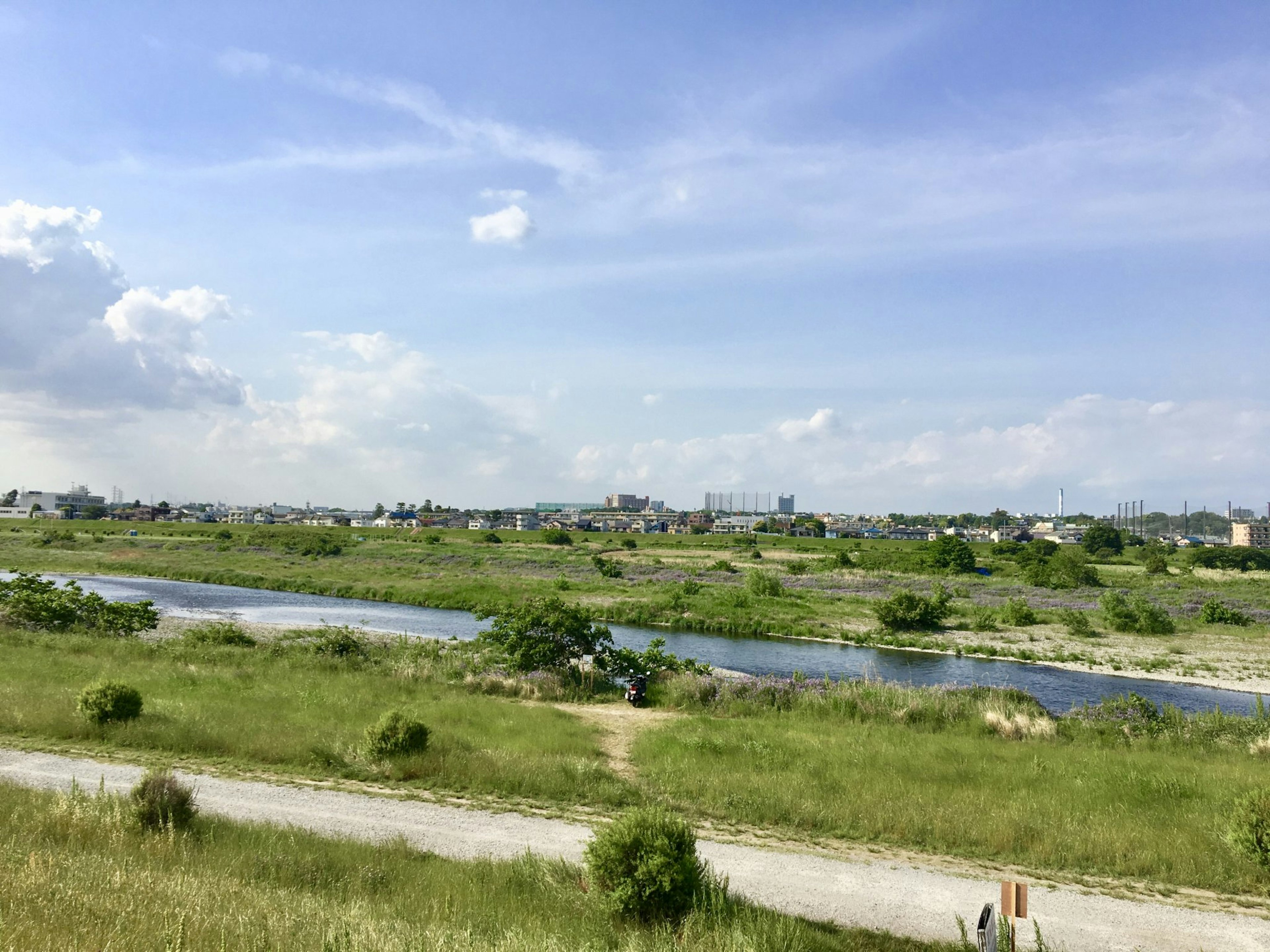 Weite grüne Felder unter einem blauen Himmel mit einem fließenden Fluss und entfernten Gebäuden