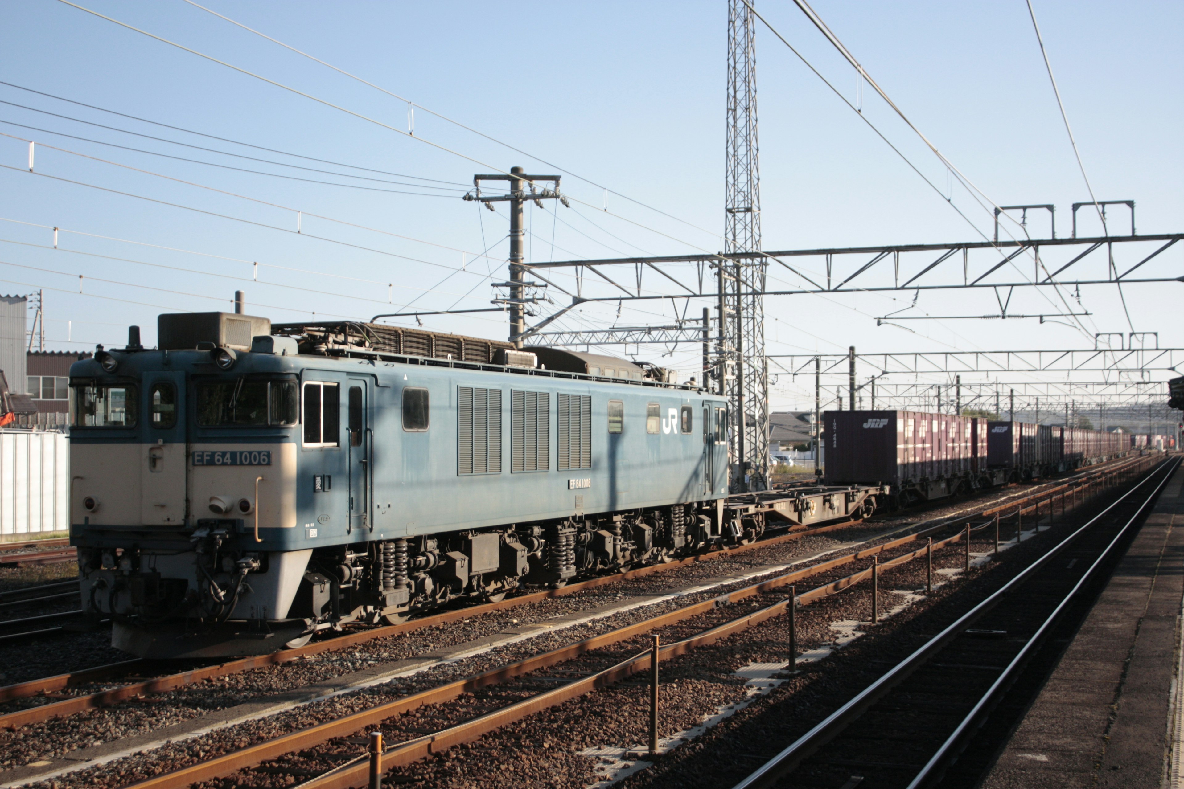 青い機関車が貨物列車を牽引している駅の風景