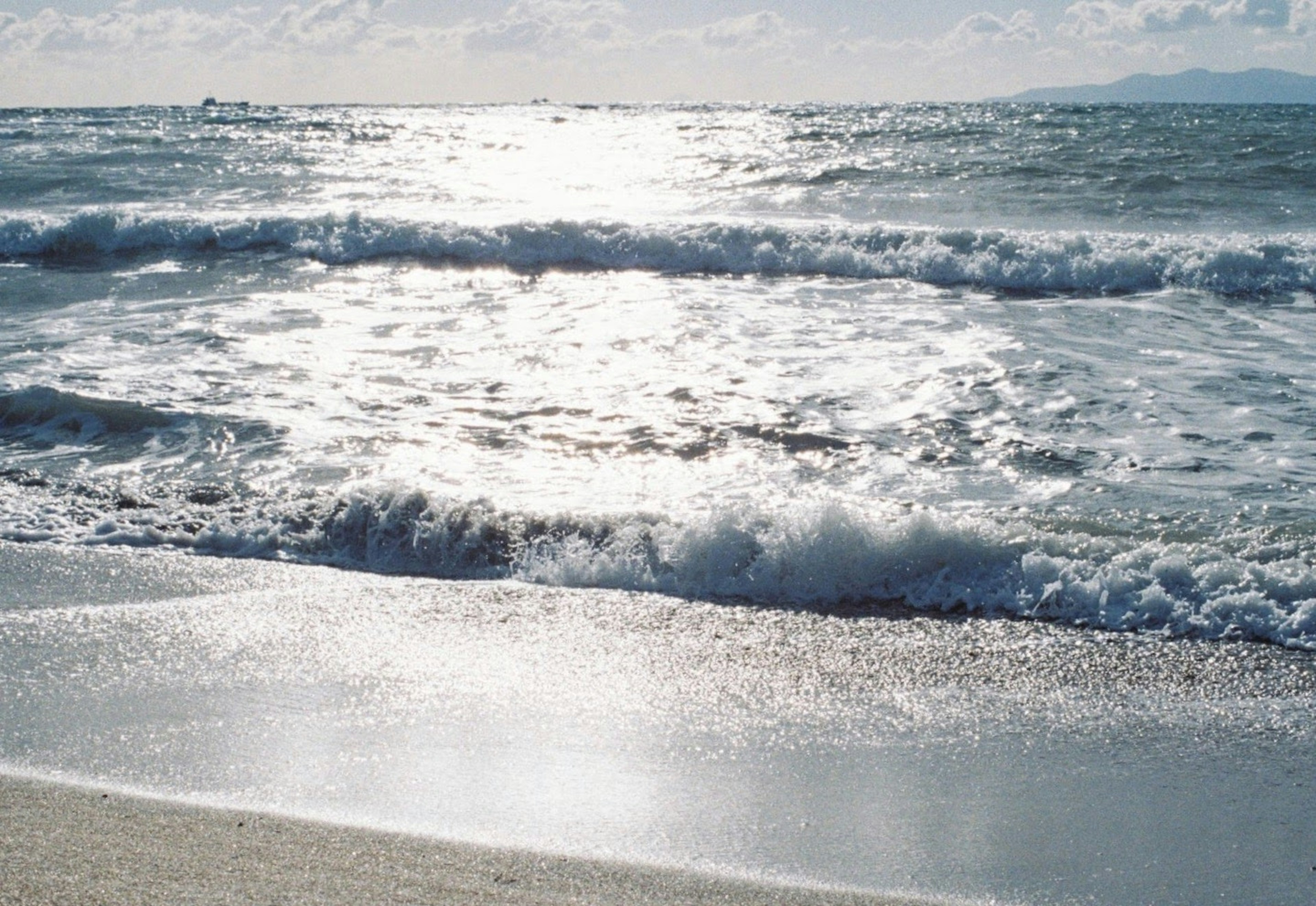 ทิวทัศน์ชายฝั่งมีคลื่นซัดสาด ชายหาดสะท้อนแสงแดดบนผิวน้ำ