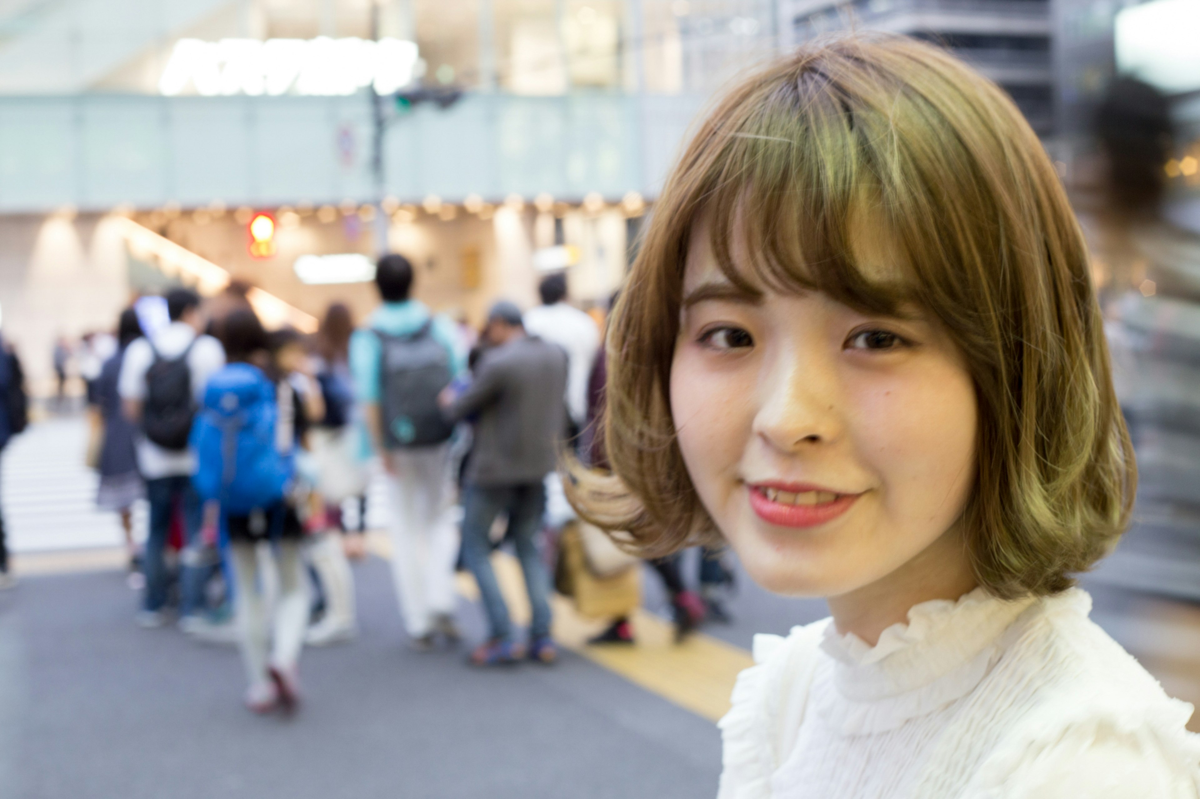 Young woman smiling while looking at the camera with people walking in the background