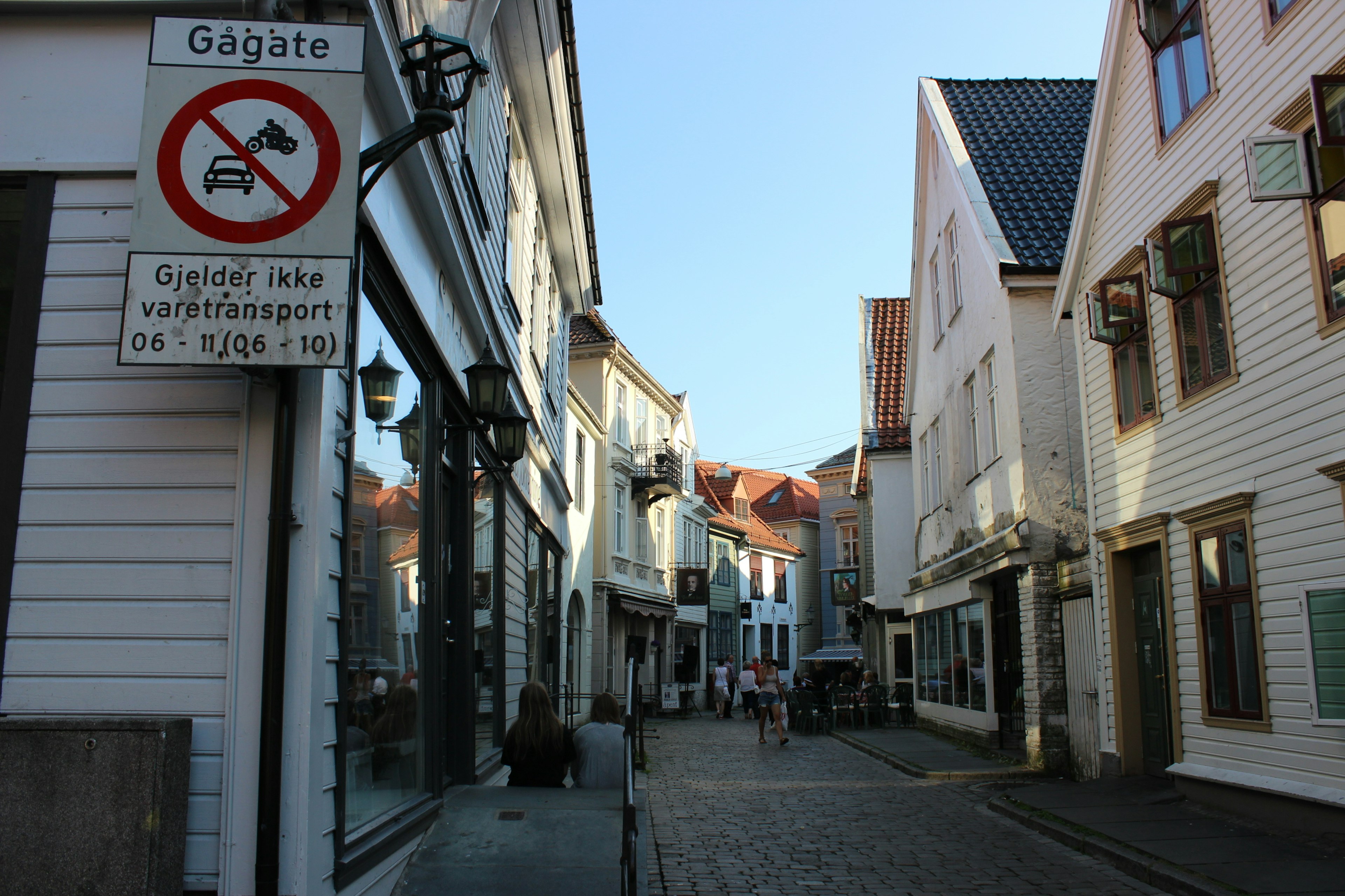 Schmale Straße gesäumt von weißen Holzbauten und blauem Himmel