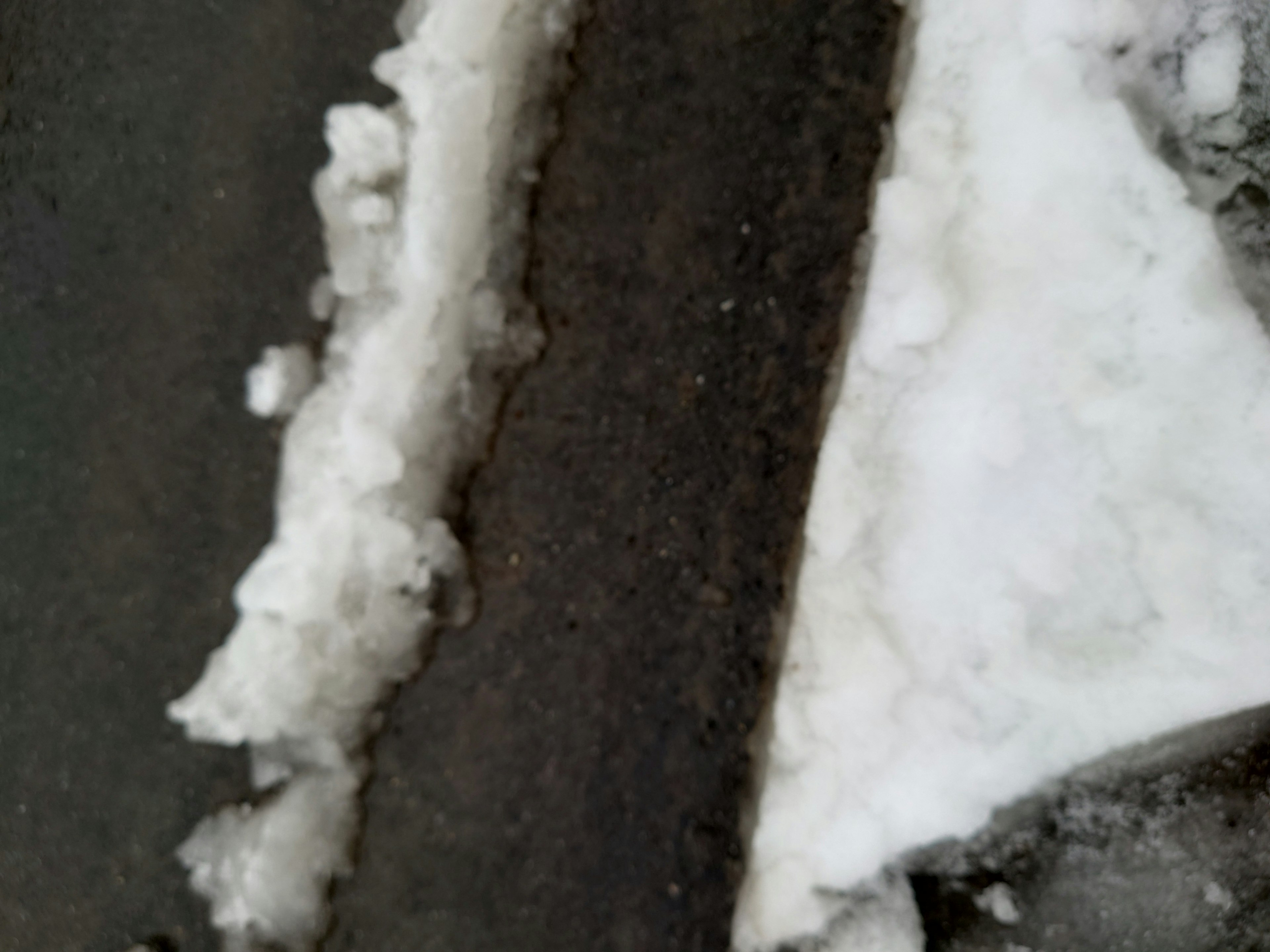 A section of a snow-covered road and dark asphalt