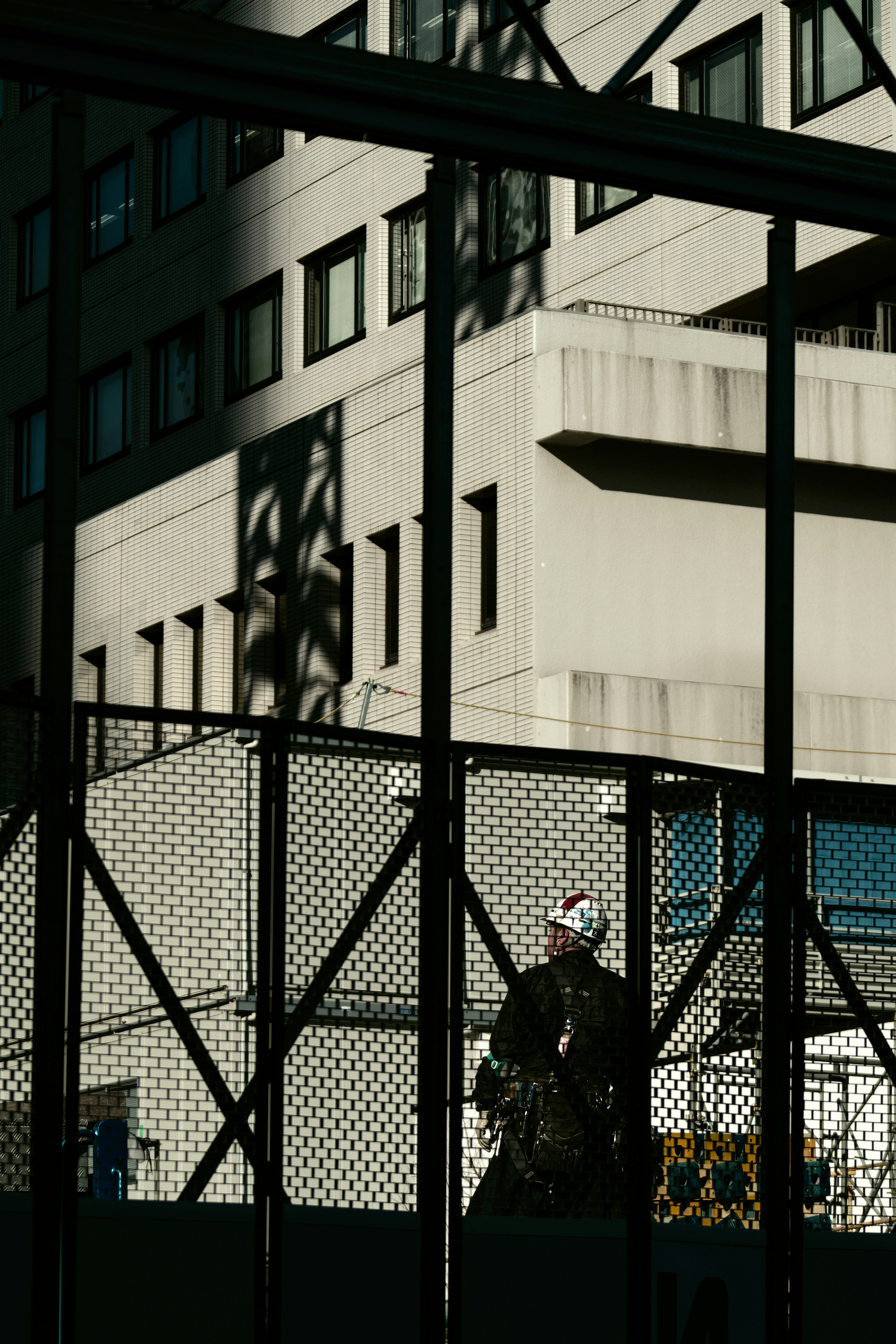 Trabajador de pie detrás de una cerca con sombras de edificios