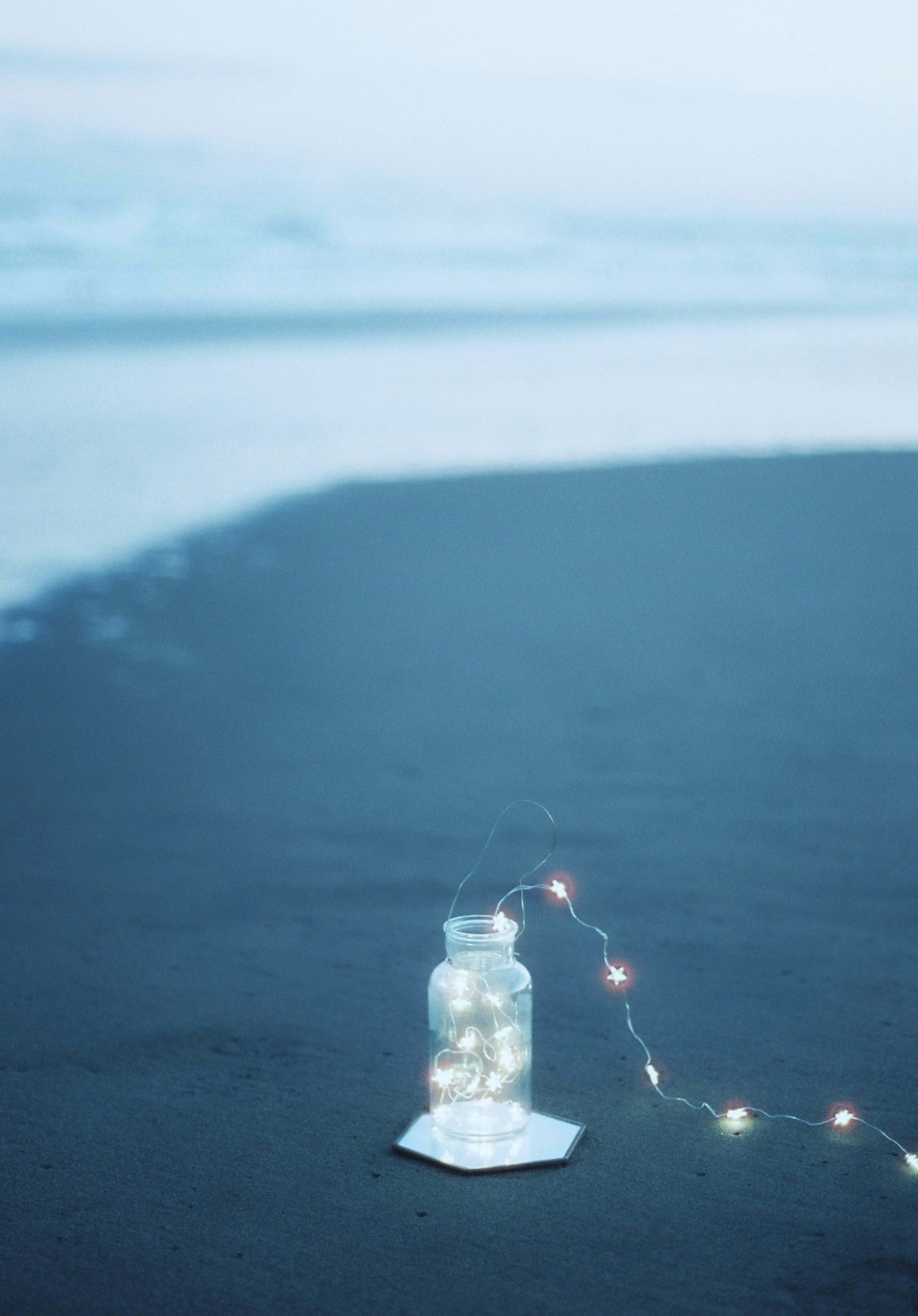 Un pot lumineux sur la plage avec une guirlande lumineuse et un fond bleu doux