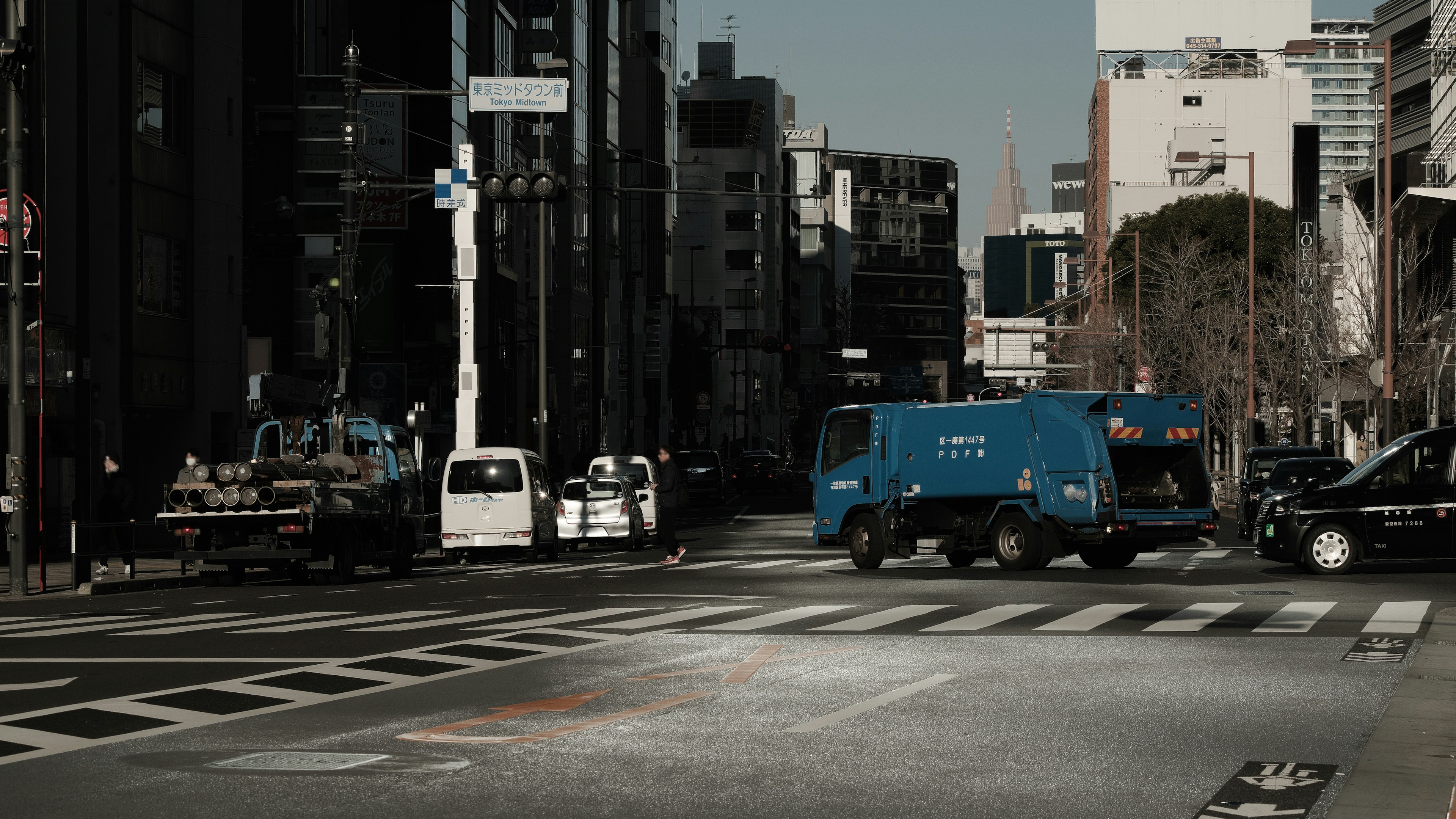 都市の交差点に停車中の青い配送車と他の車両