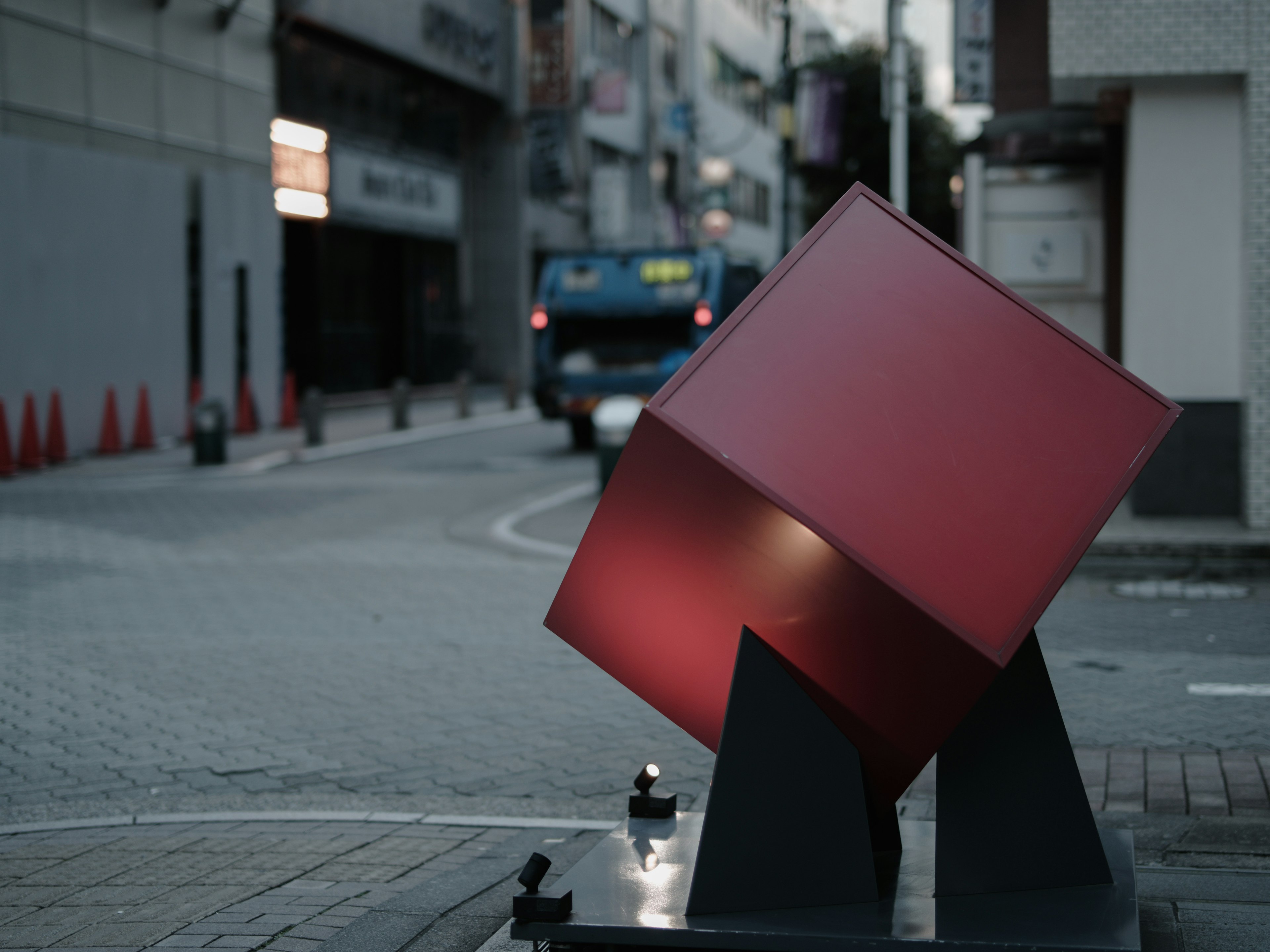 Une sculpture en cube rouge placée à un coin de rue avec un bus en arrière-plan