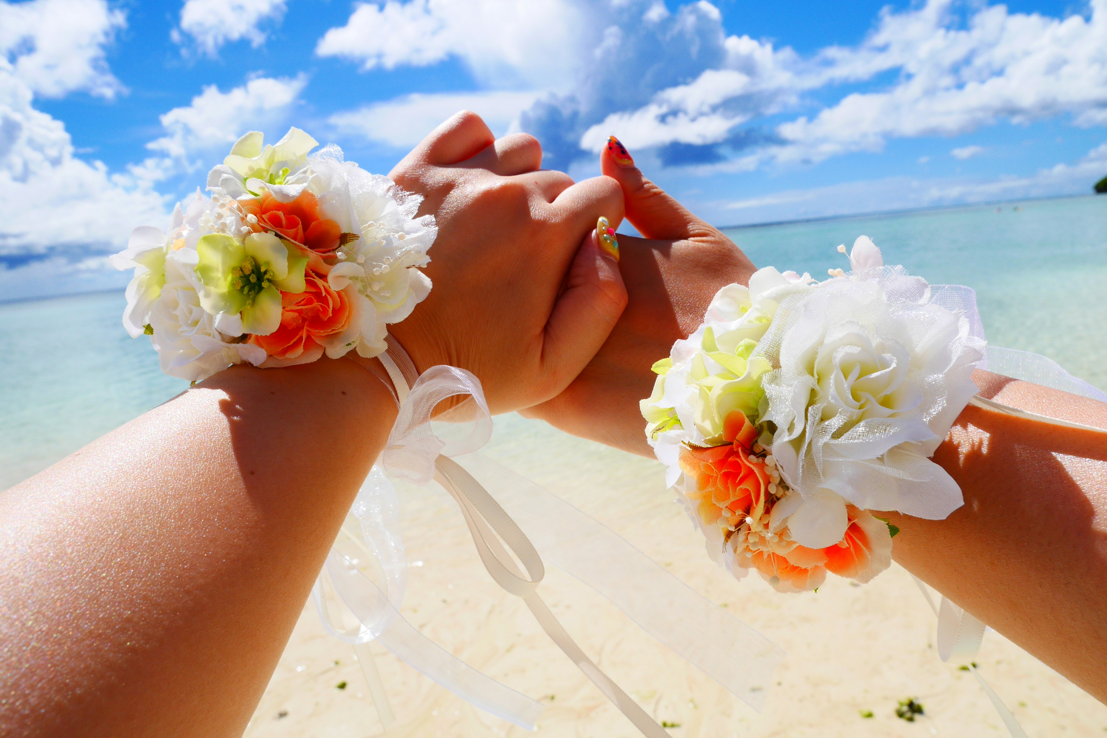 青い空と海の背景に花のブレスレットをつけた手