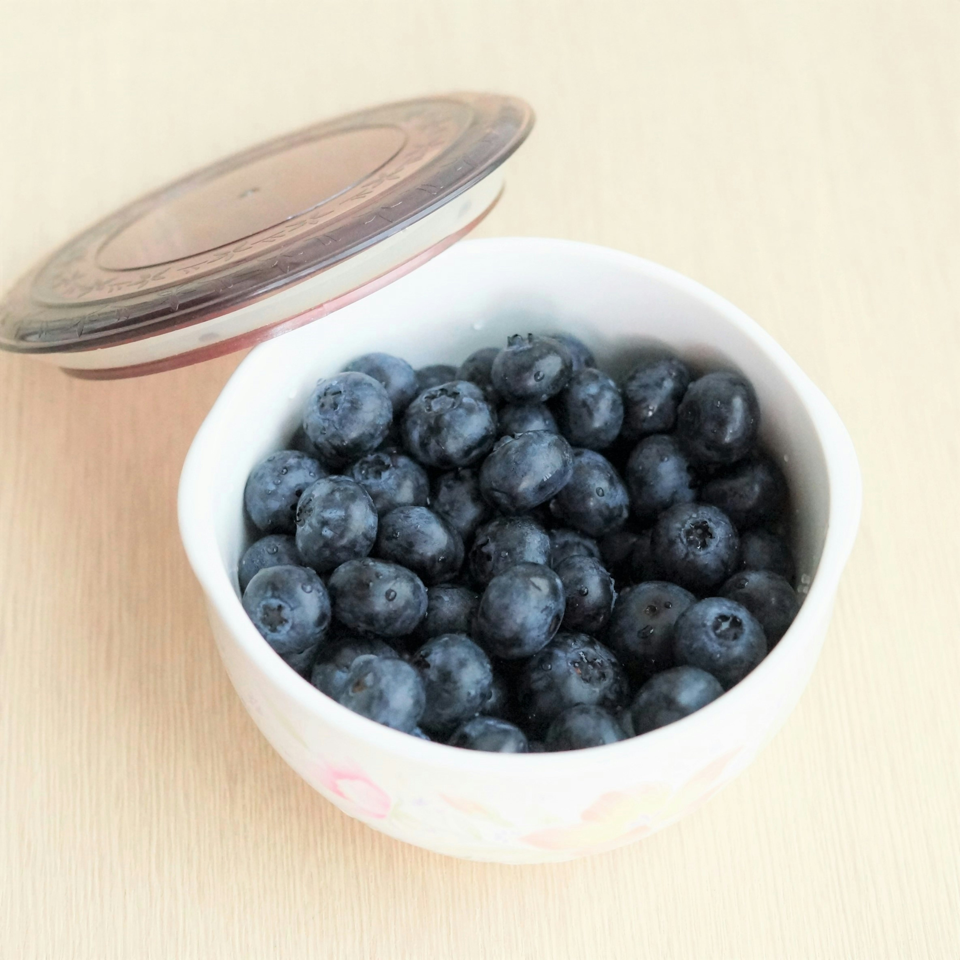 A white ceramic bowl filled with fresh blueberries topped with a lid