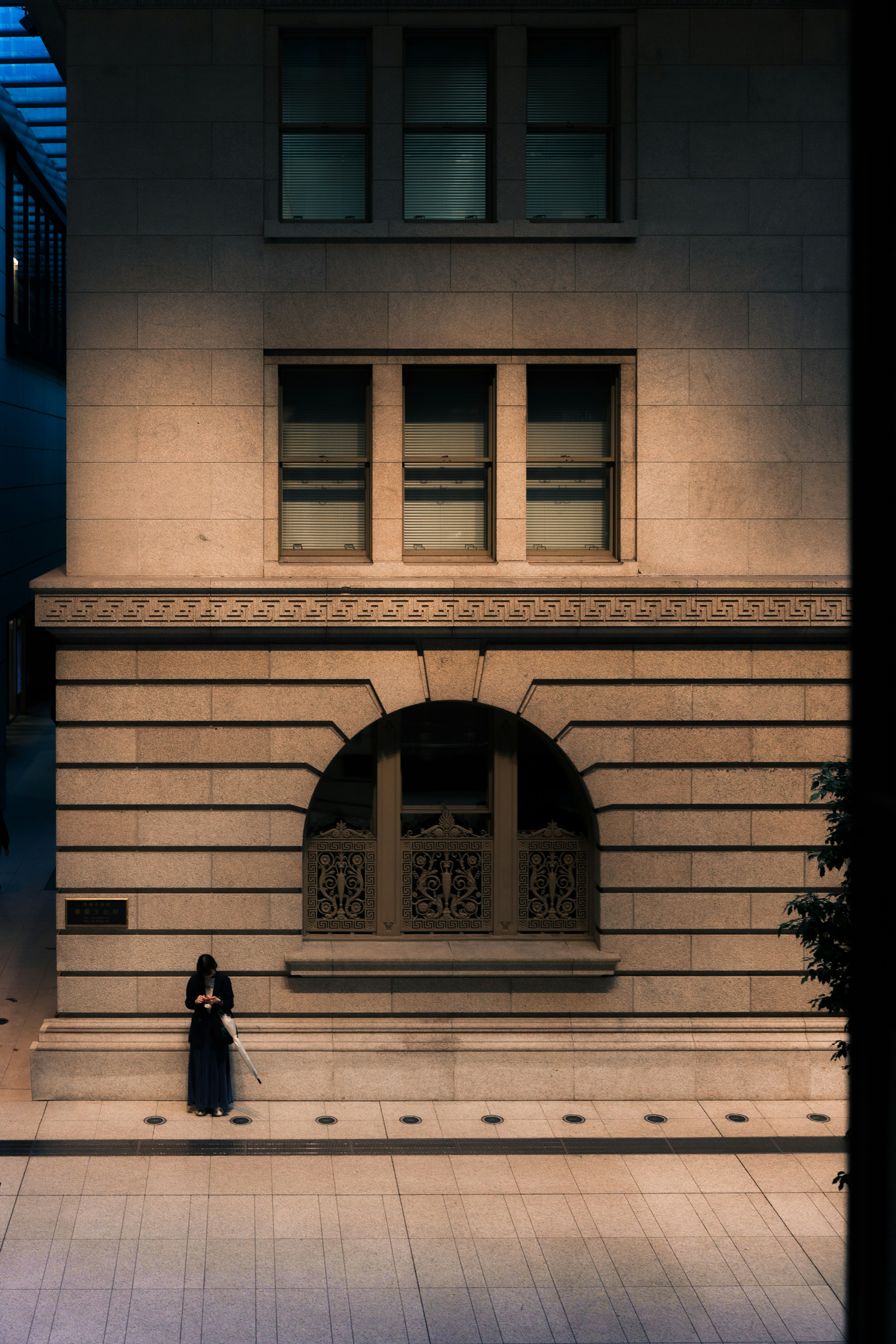 A woman sitting in front of a building with beautiful lighting and window design