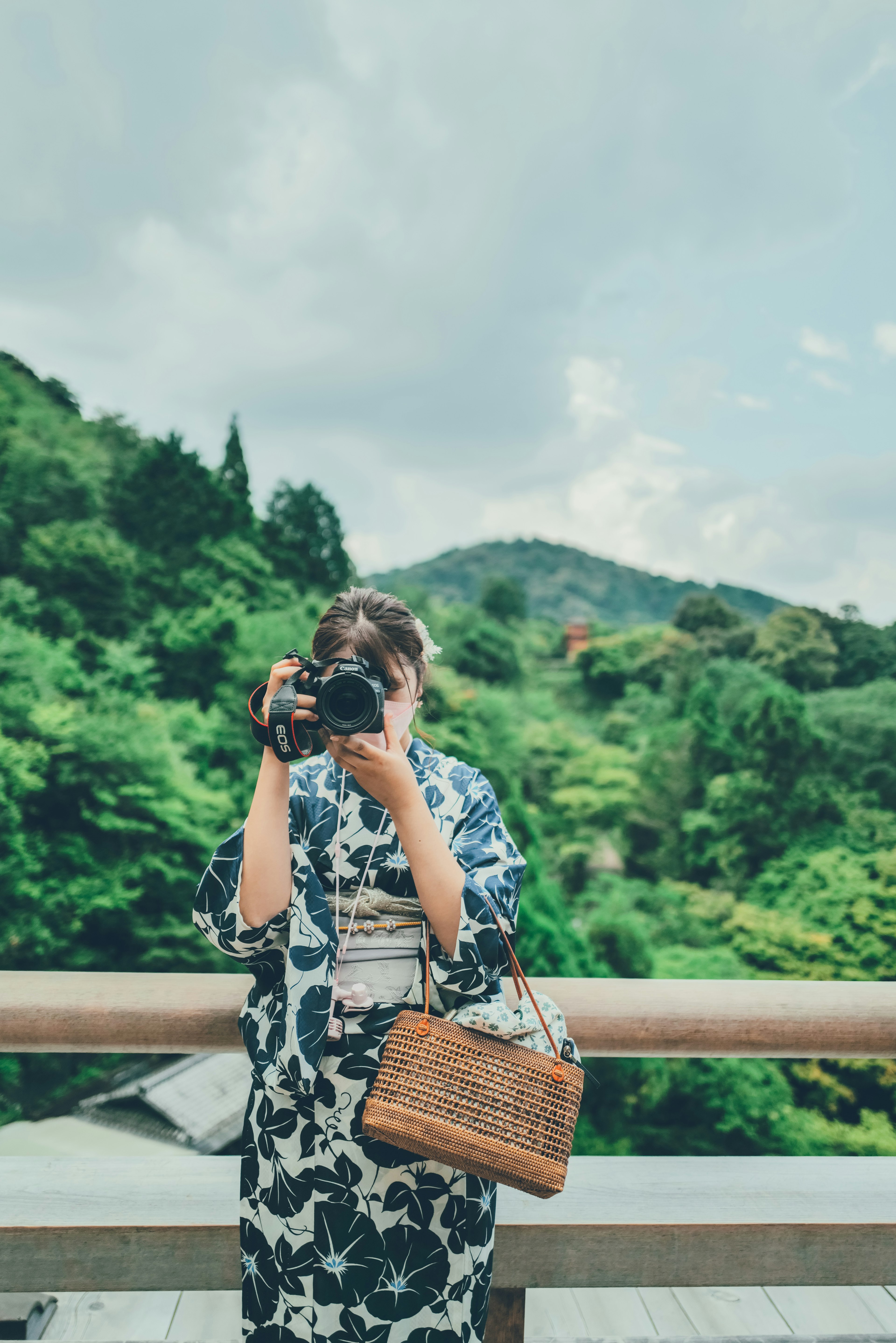 Mujer con kimono floral azul sosteniendo una cámara con un fondo verde exuberante