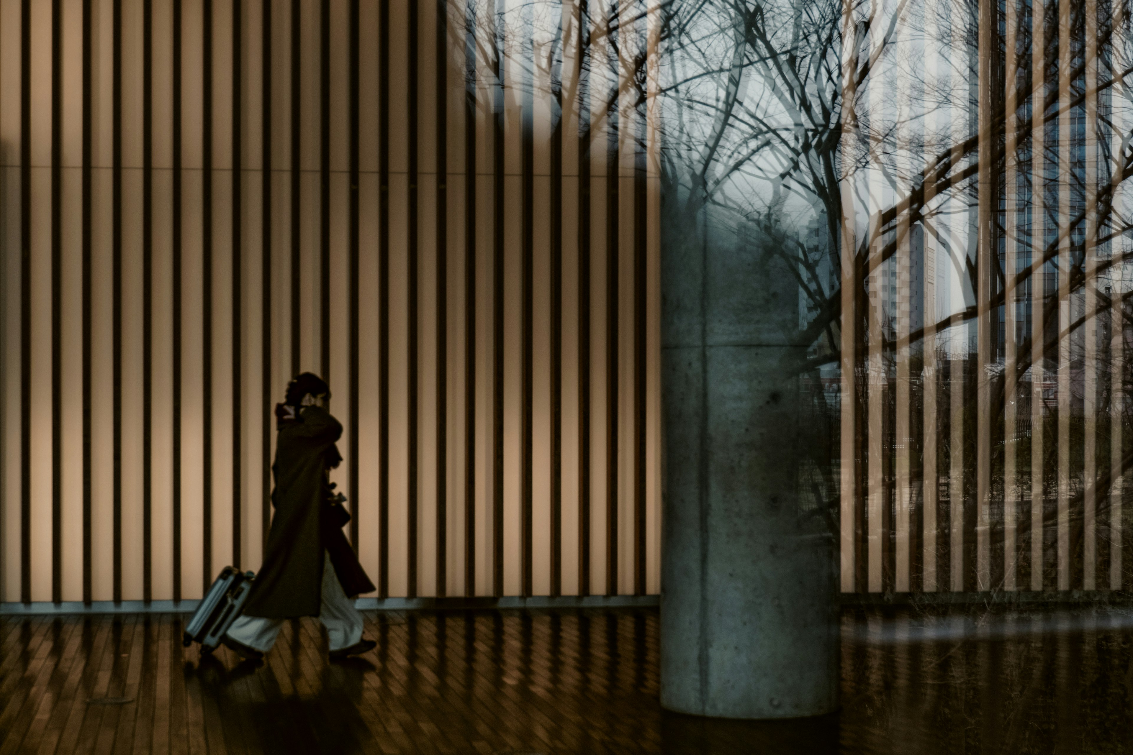 A person pulling a suitcase in a modern building interior with wooden slats