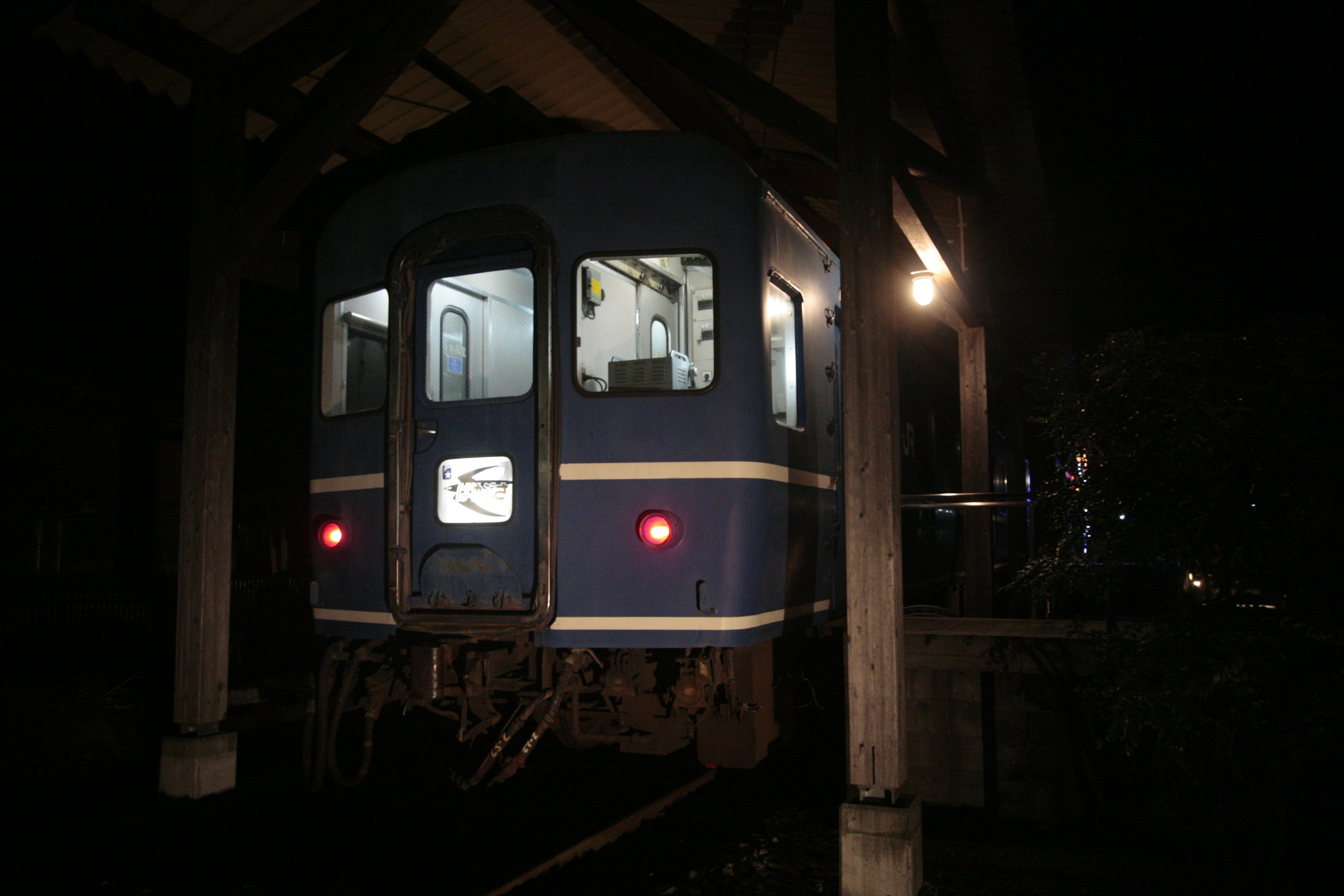 A blue train viewed from the back at night with dim lighting