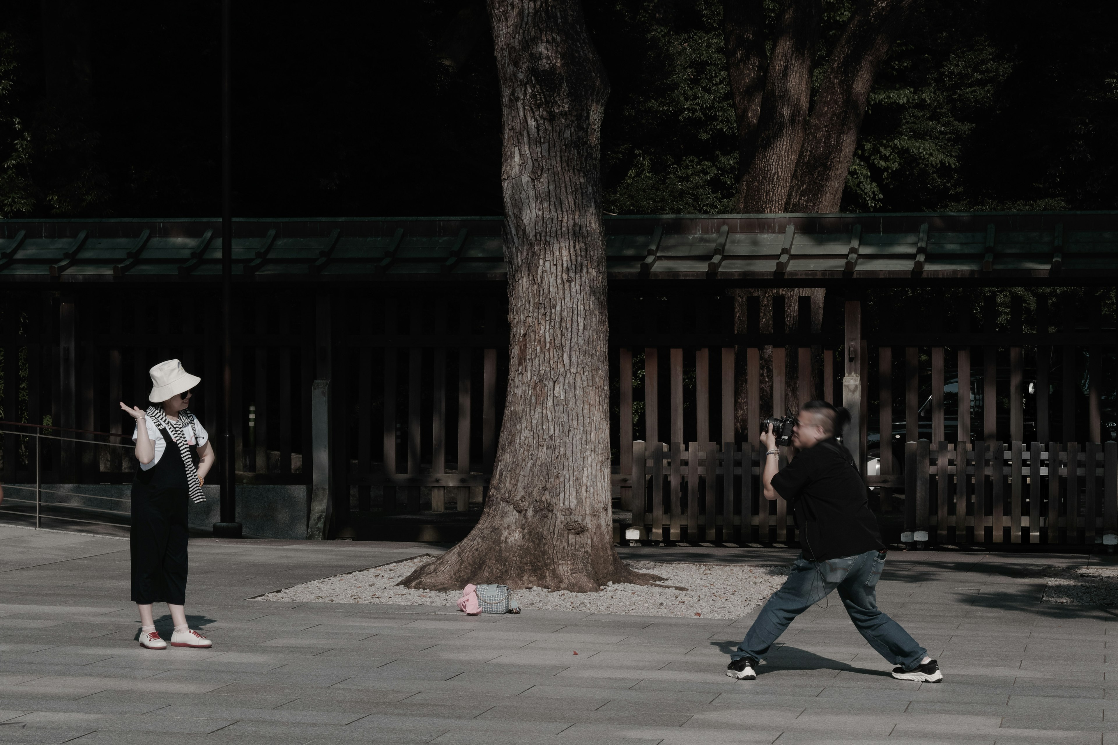 Two people posing in front of a tree a woman in a white hat and a man holding a camera