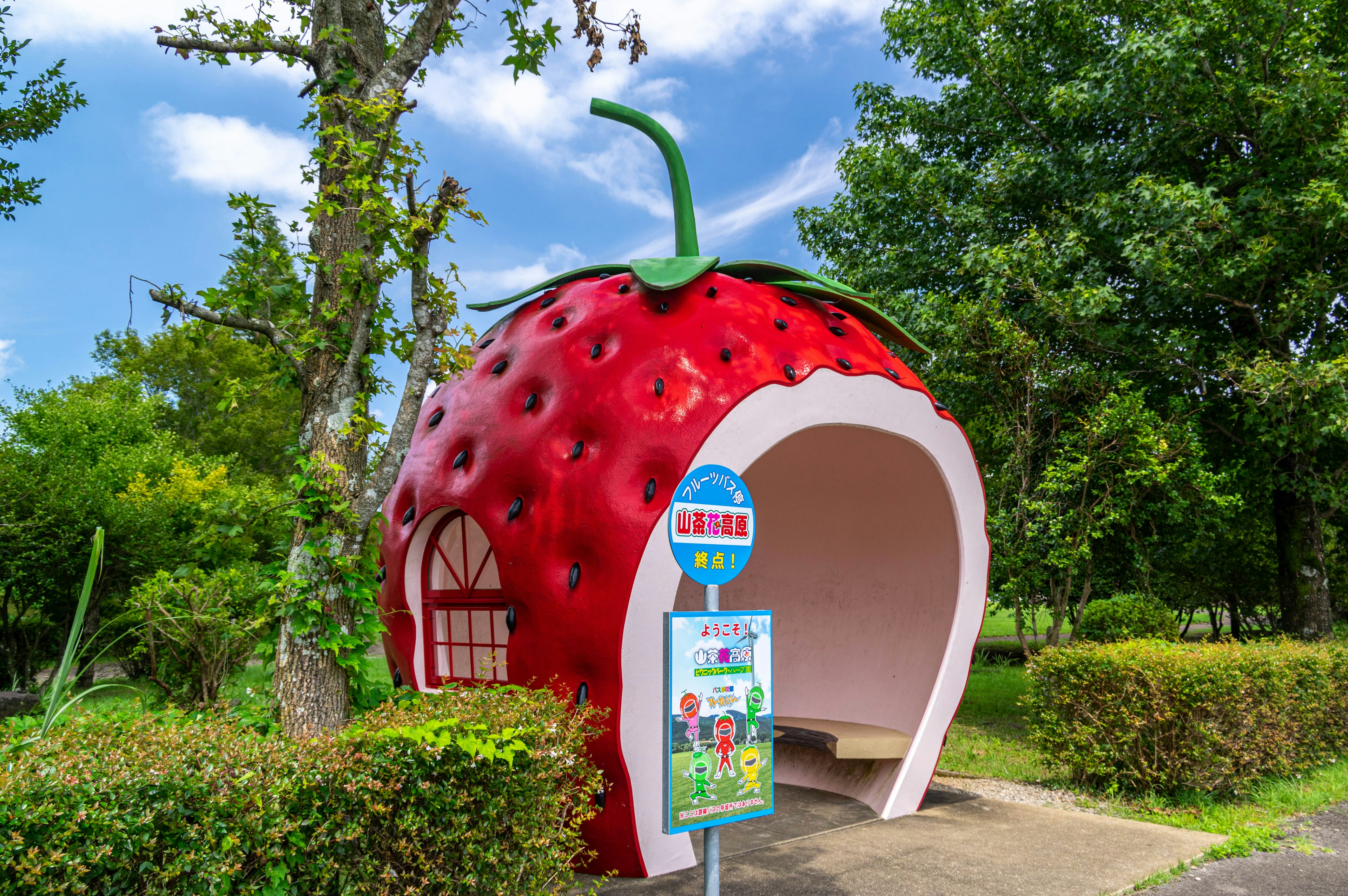 Area di riposo unica a forma di fragola circondata da alberi verdi e cielo blu