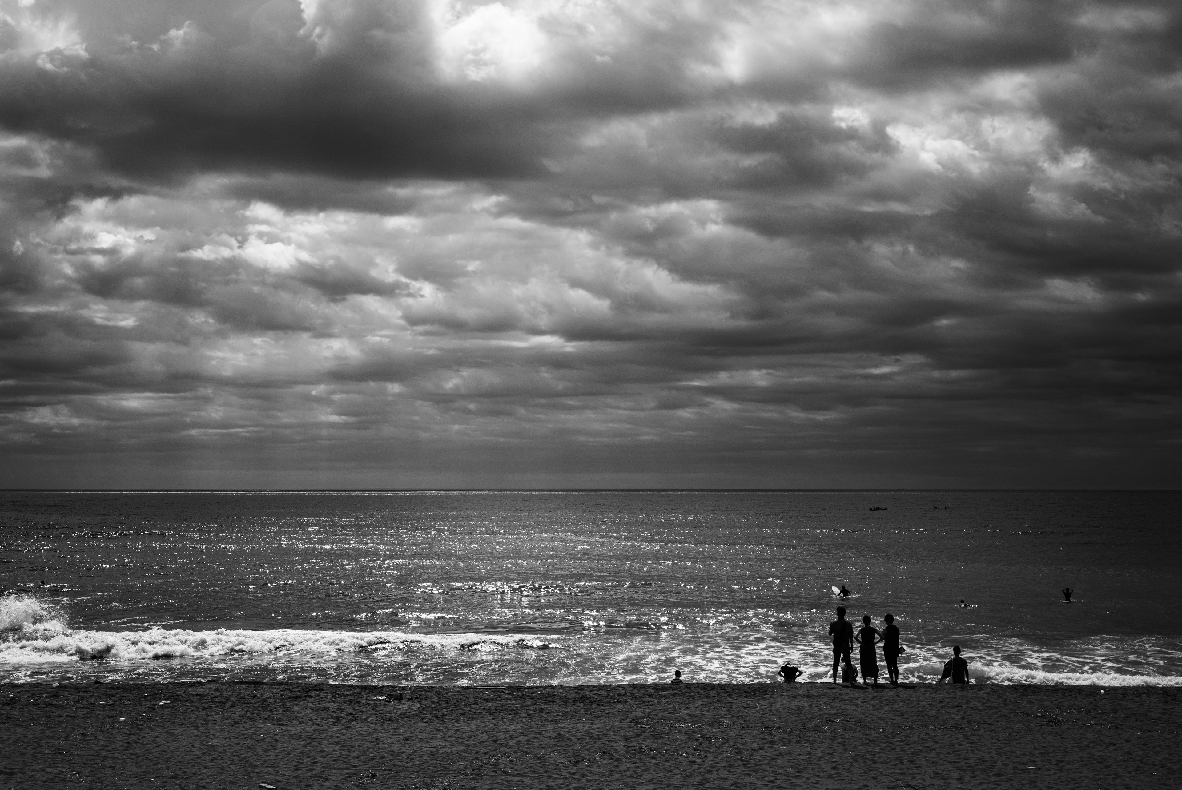 Menschen stehen am Strand unter einem bewölkten Himmel mit sanften Wellen