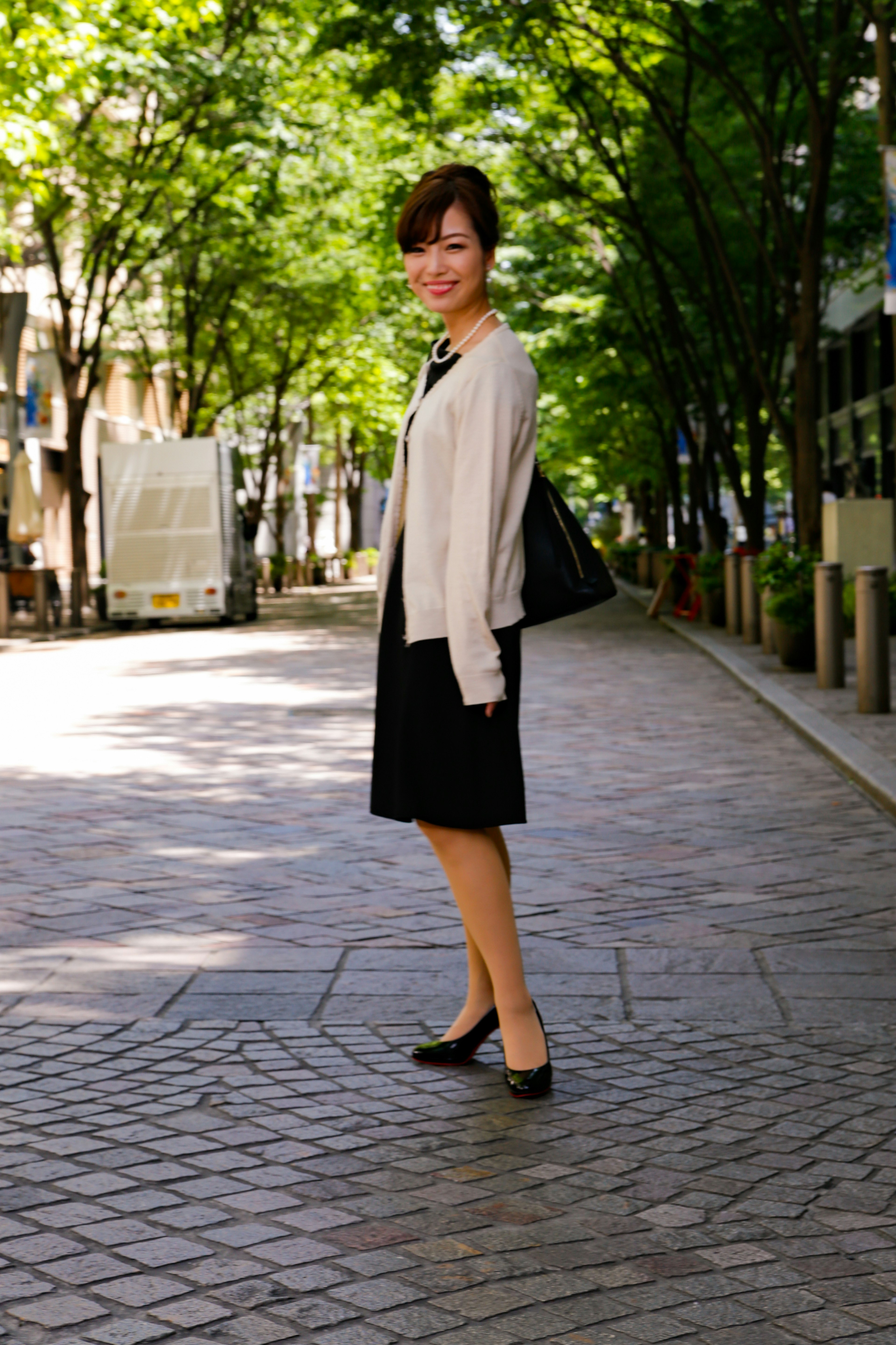 A woman standing on a street surrounded by green trees and cobblestone pavement