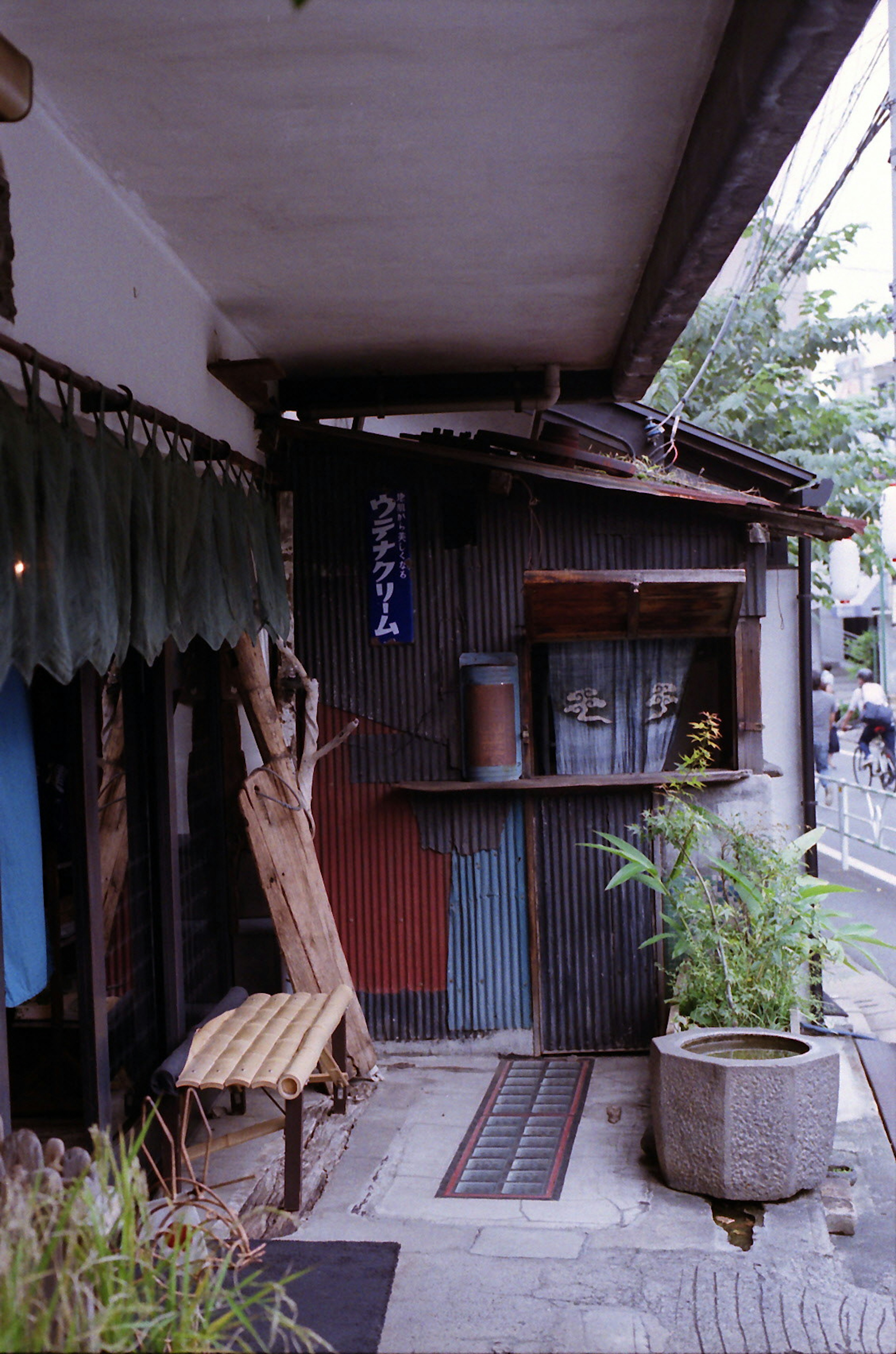 Exterior of an old shop facing a narrow street with a tiled roof wooden bench and potted plants