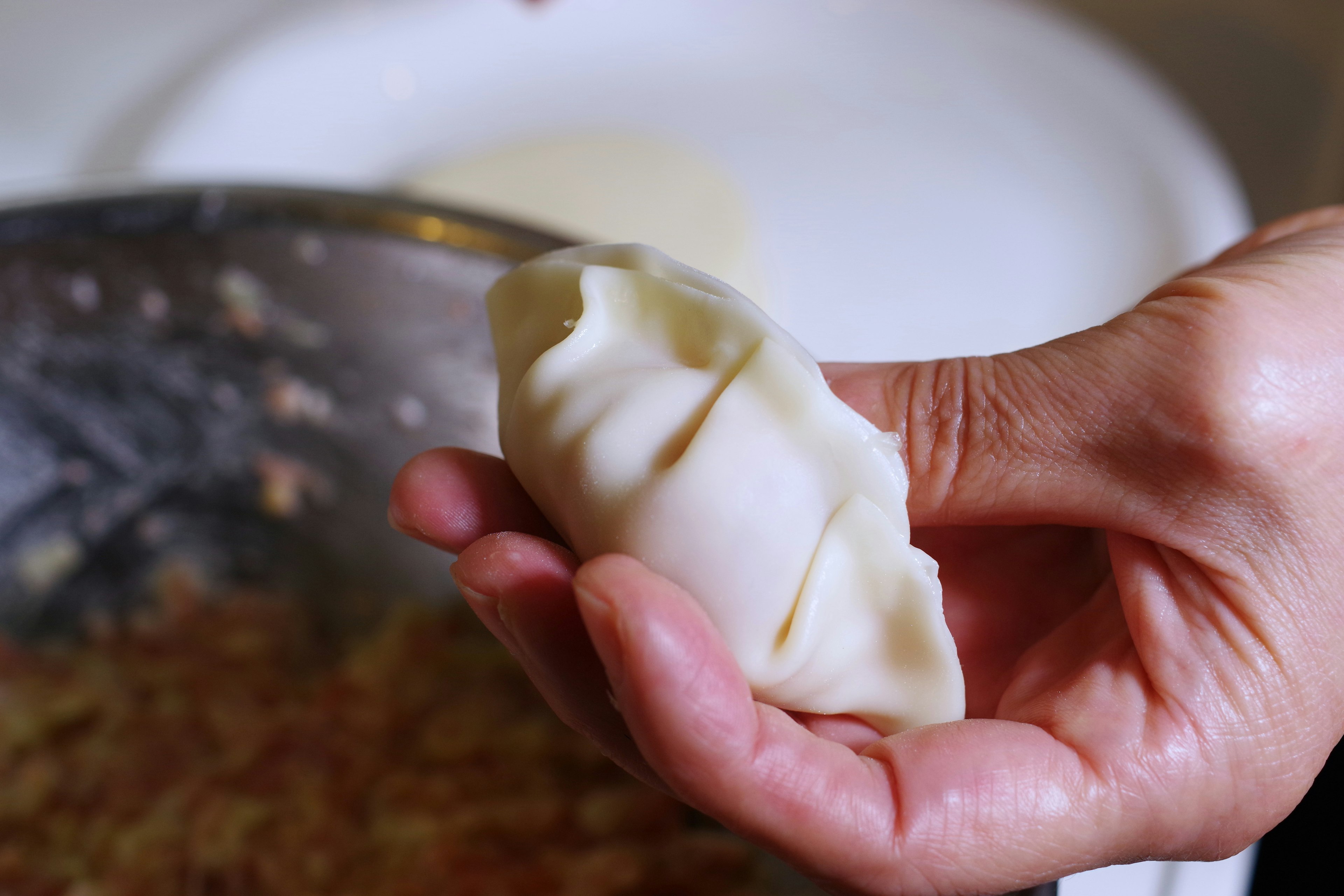 A hand holding a dumpling filled with ingredients in a cooking scene