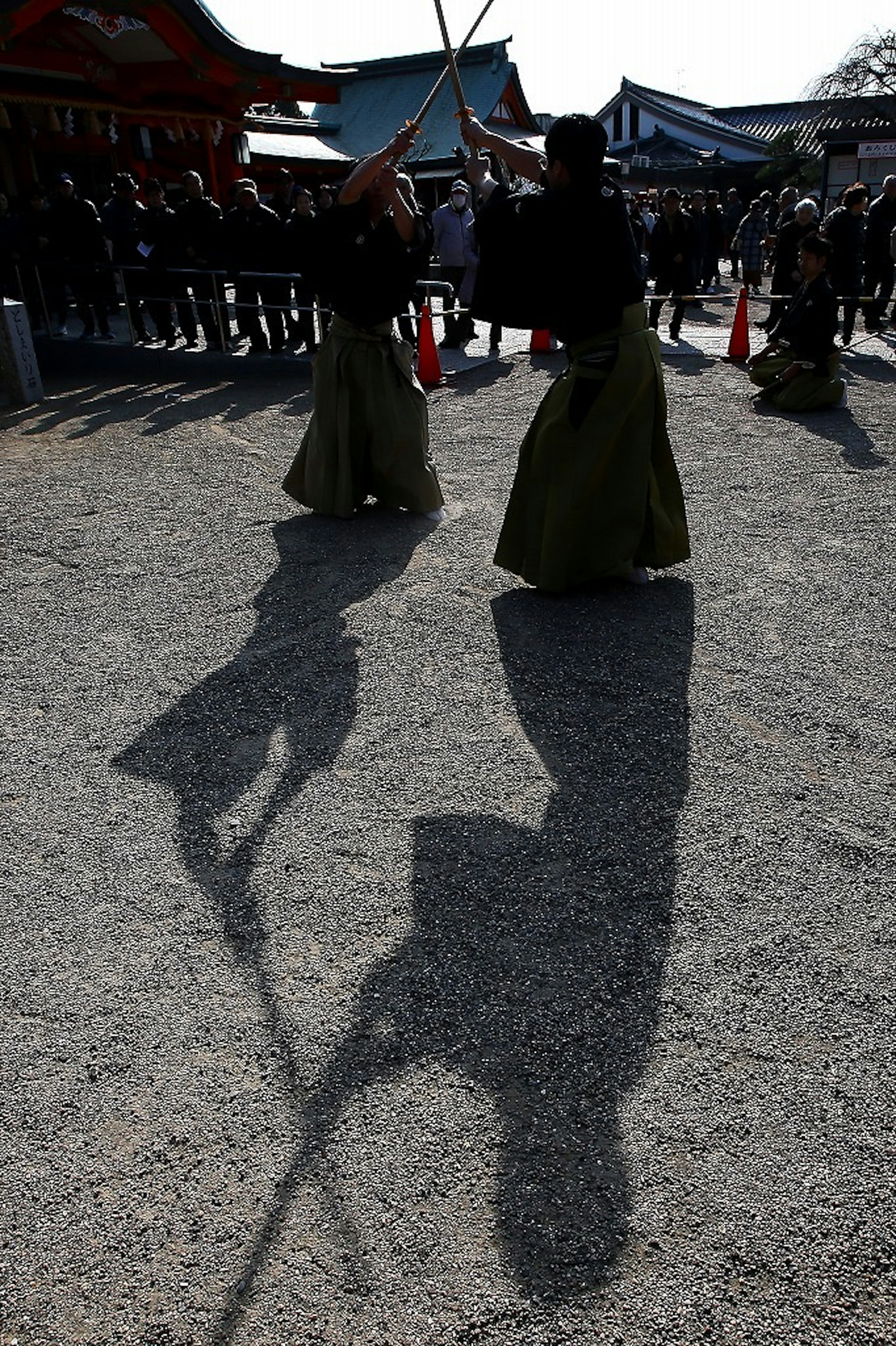 Two swordsmen performing a martial arts demonstration with their shadows visible on the ground