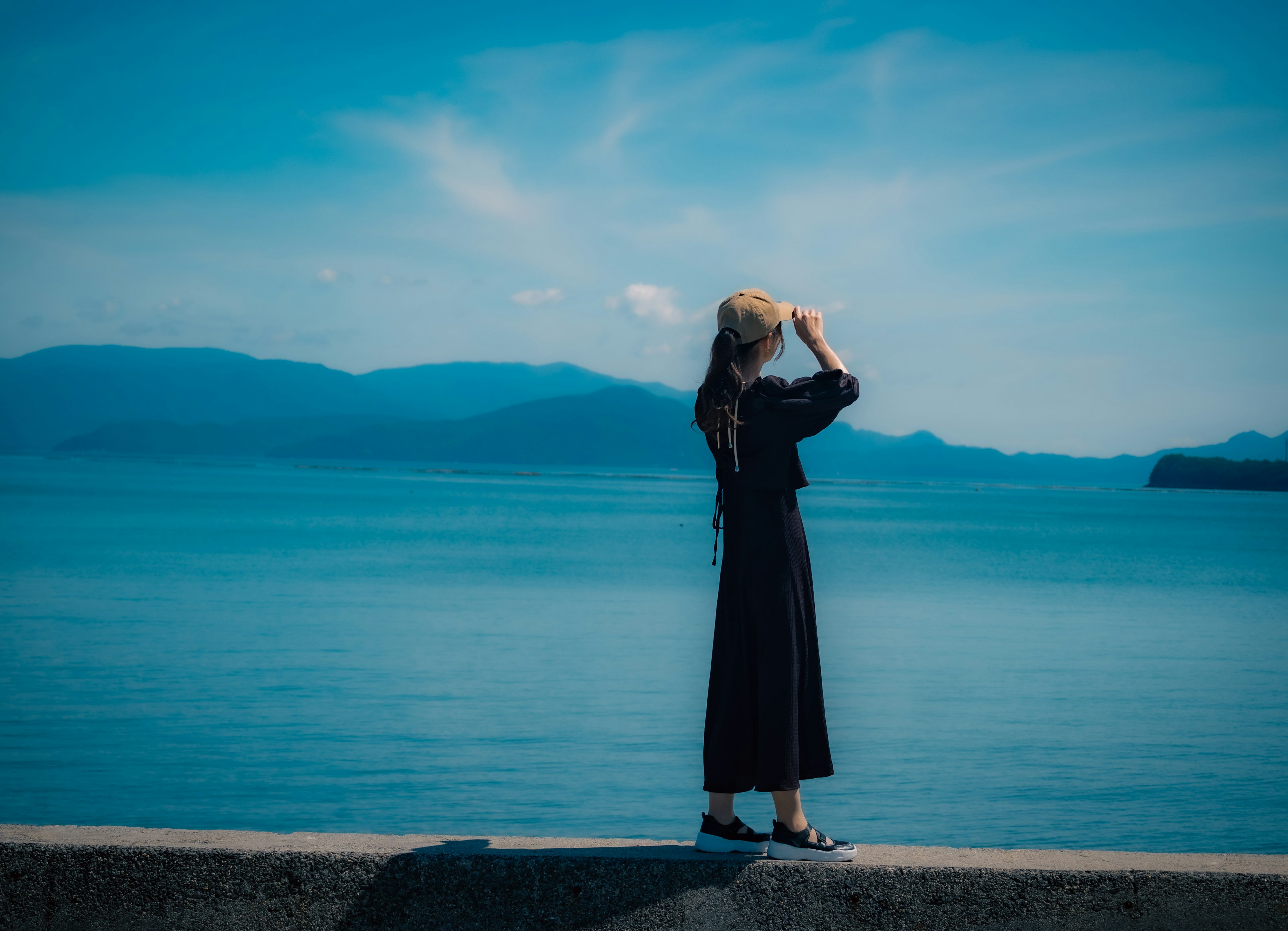 Silhouette einer Frau, die auf das blaue Meer schaut, trägt ein schwarzes Kleid