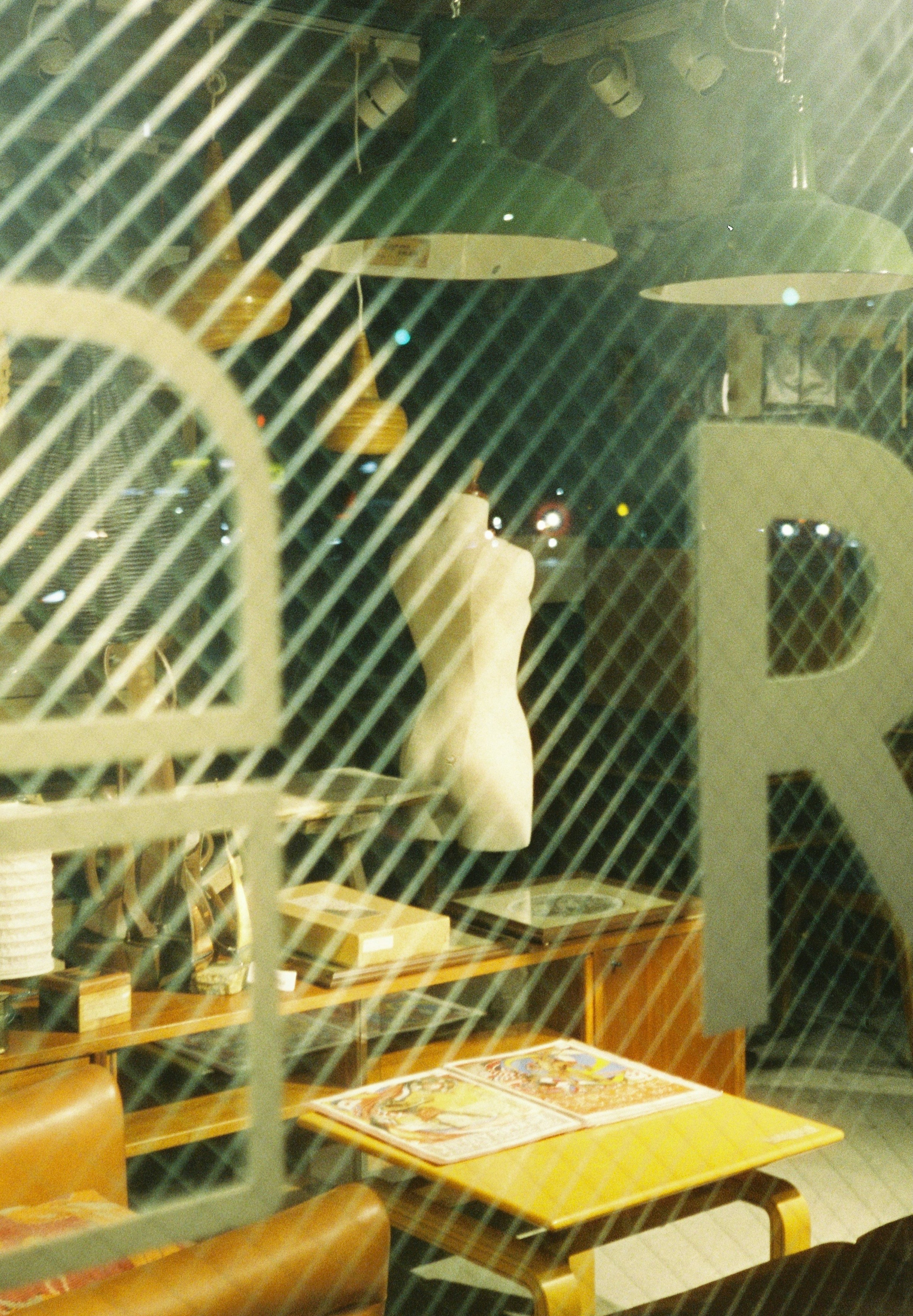 View of a cafe interior through a window featuring a clothing mannequin and a table