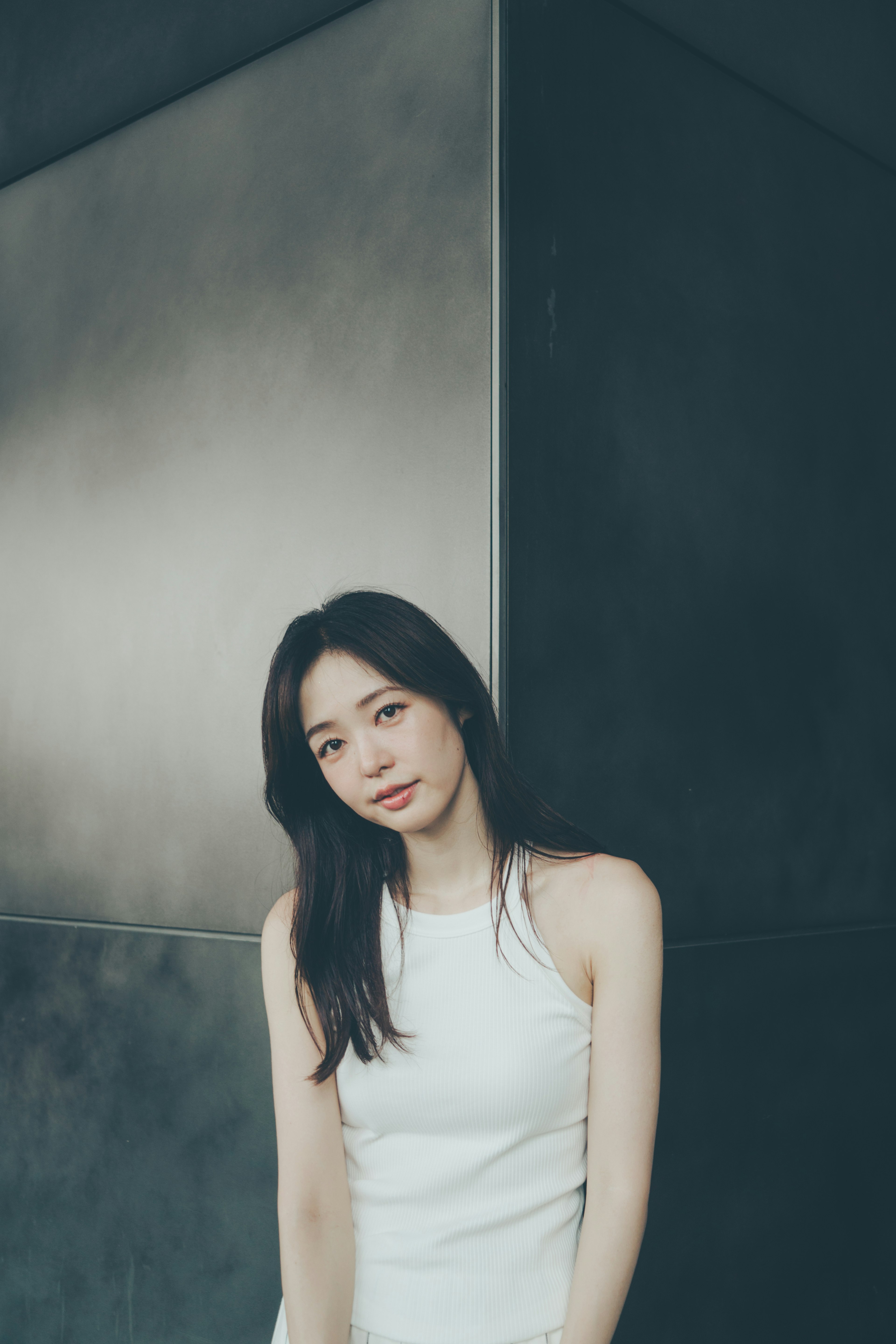 Una mujer con un vestido blanco está de pie frente a una pared con un fondo simple y elegante