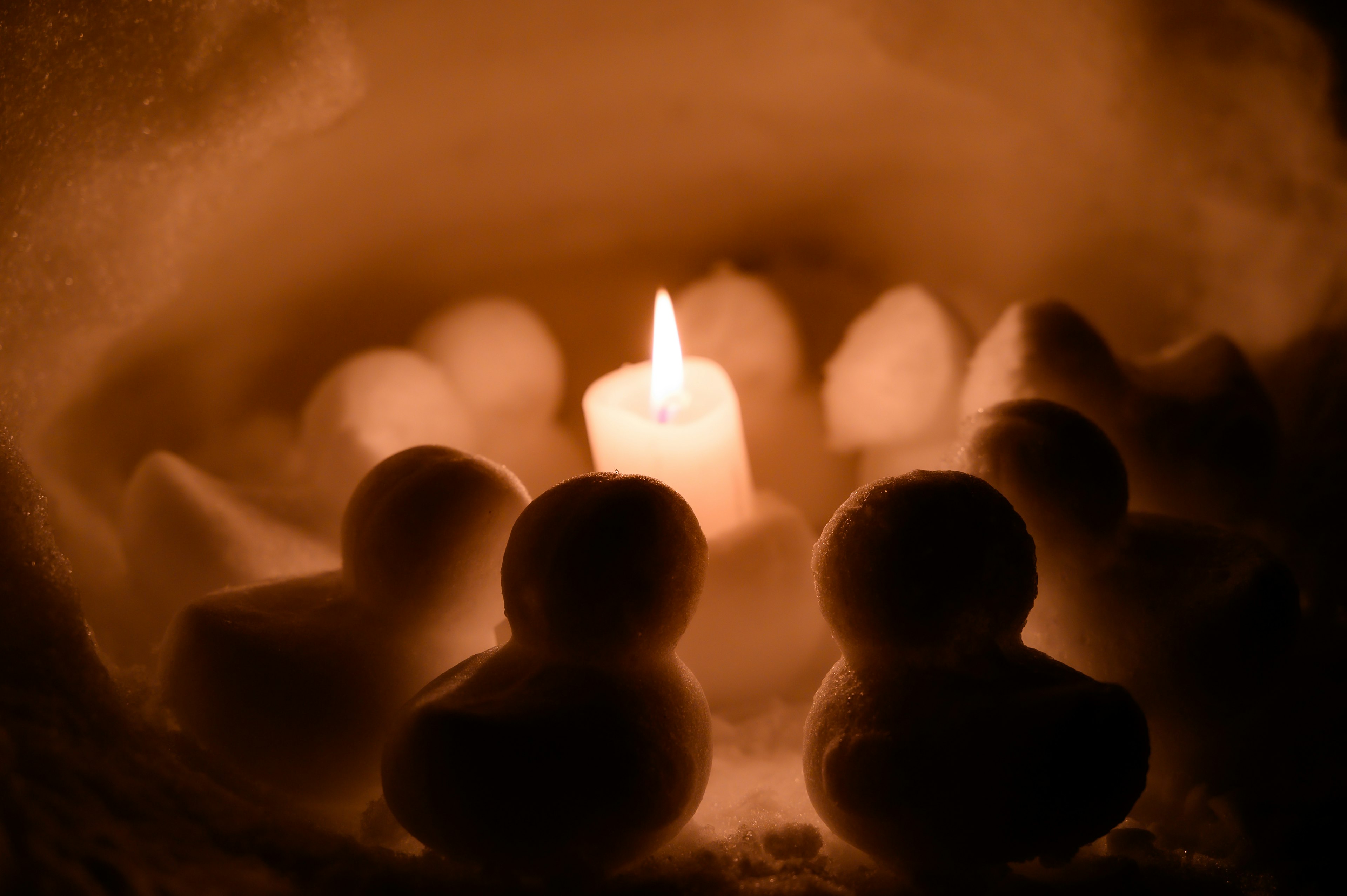 Snowmen arranged around a glowing candle in a snowy setting